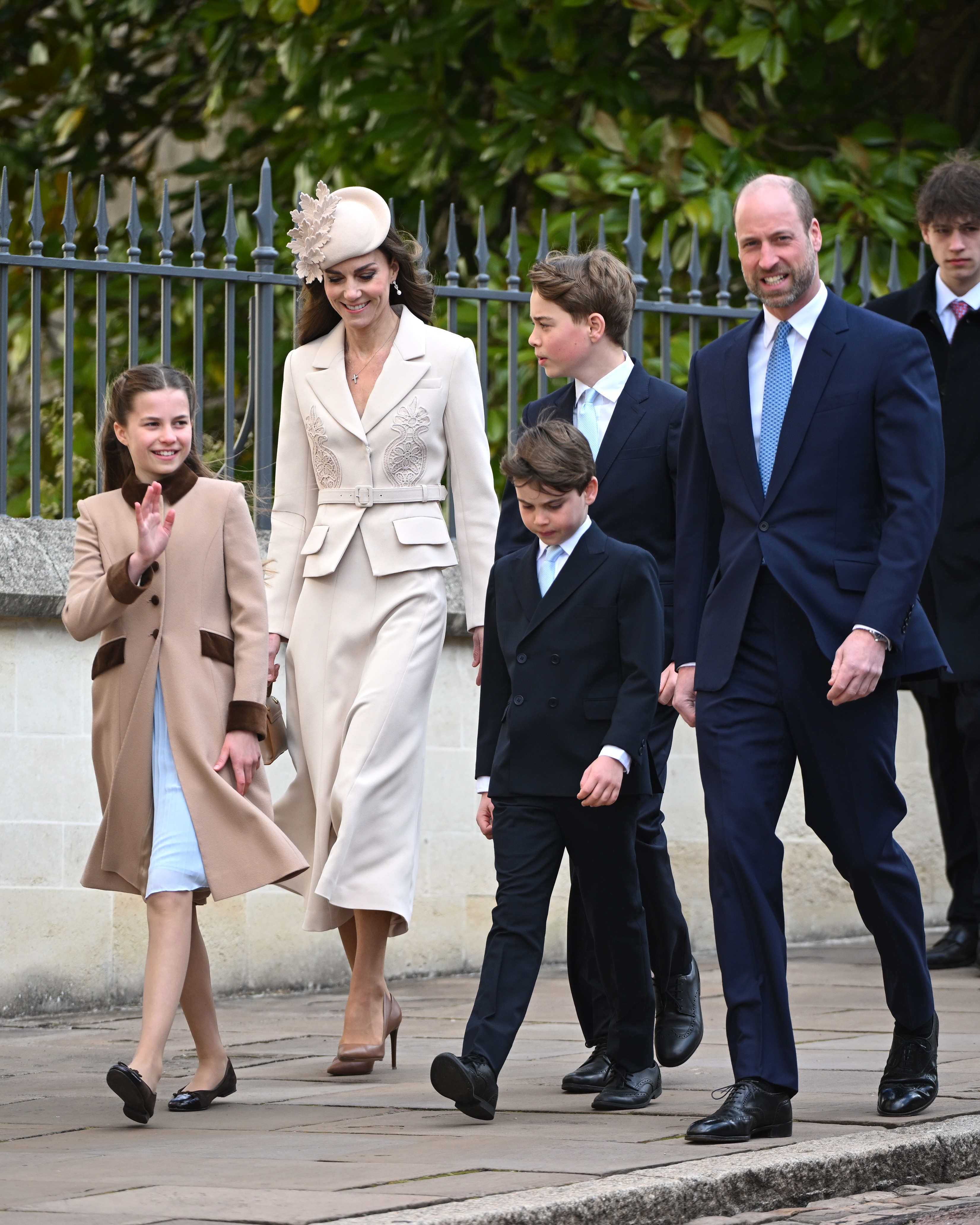 The full Wales family together in one frame as they make their way towards St George's Chapel on Easter Sunday, each of the five caught mid-stride in the April light. Princess Charlotte waves to the crowds on the left while Prince Louis walks between his parents, and Prince George, already towering above his younger brother, is visible just behind the Princess of Wales.