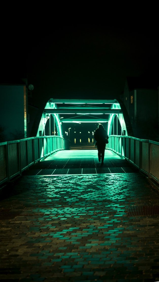 Mujer caminando sola por un puente de la ciudad en la noche. | Foto: Unsplash