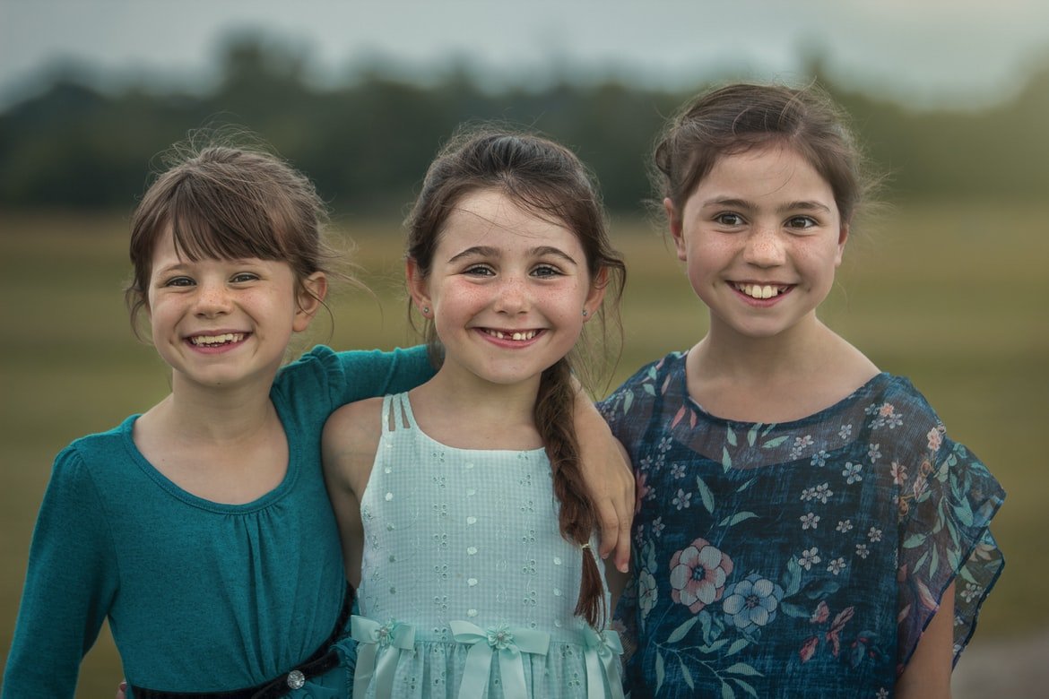 Tres niñas sonriendo mientras posan en un campo. | Foto: Unsplash