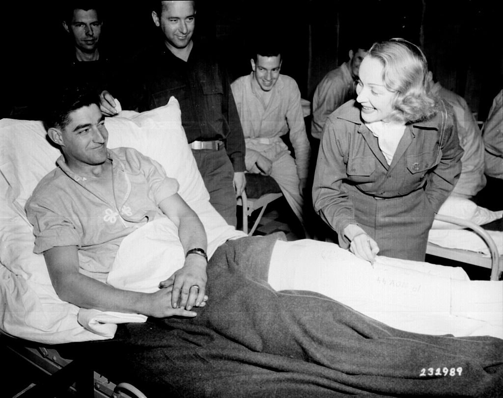 Marlene Dietrich autographs the cast on the leg of Tec 4 Earl E. McFarland of Cavider, Texas, on November 24, 1944 at a United States hospital in Belgium, where she has been entertaining the G.Is'. | Photo: NARA - 531330, WikiMedia 