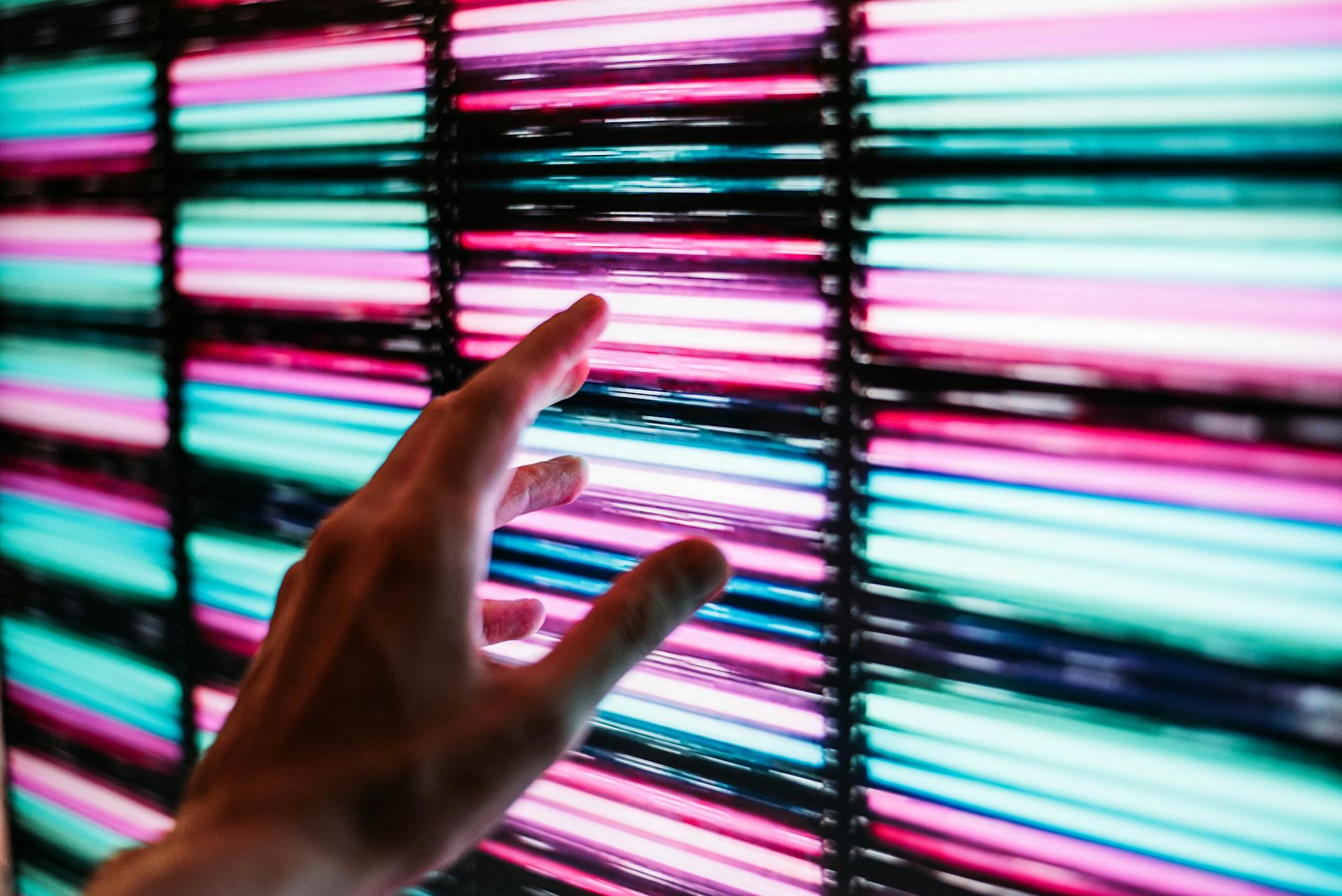 A person about to touch a blue and pink LED panel | Source: Pexels