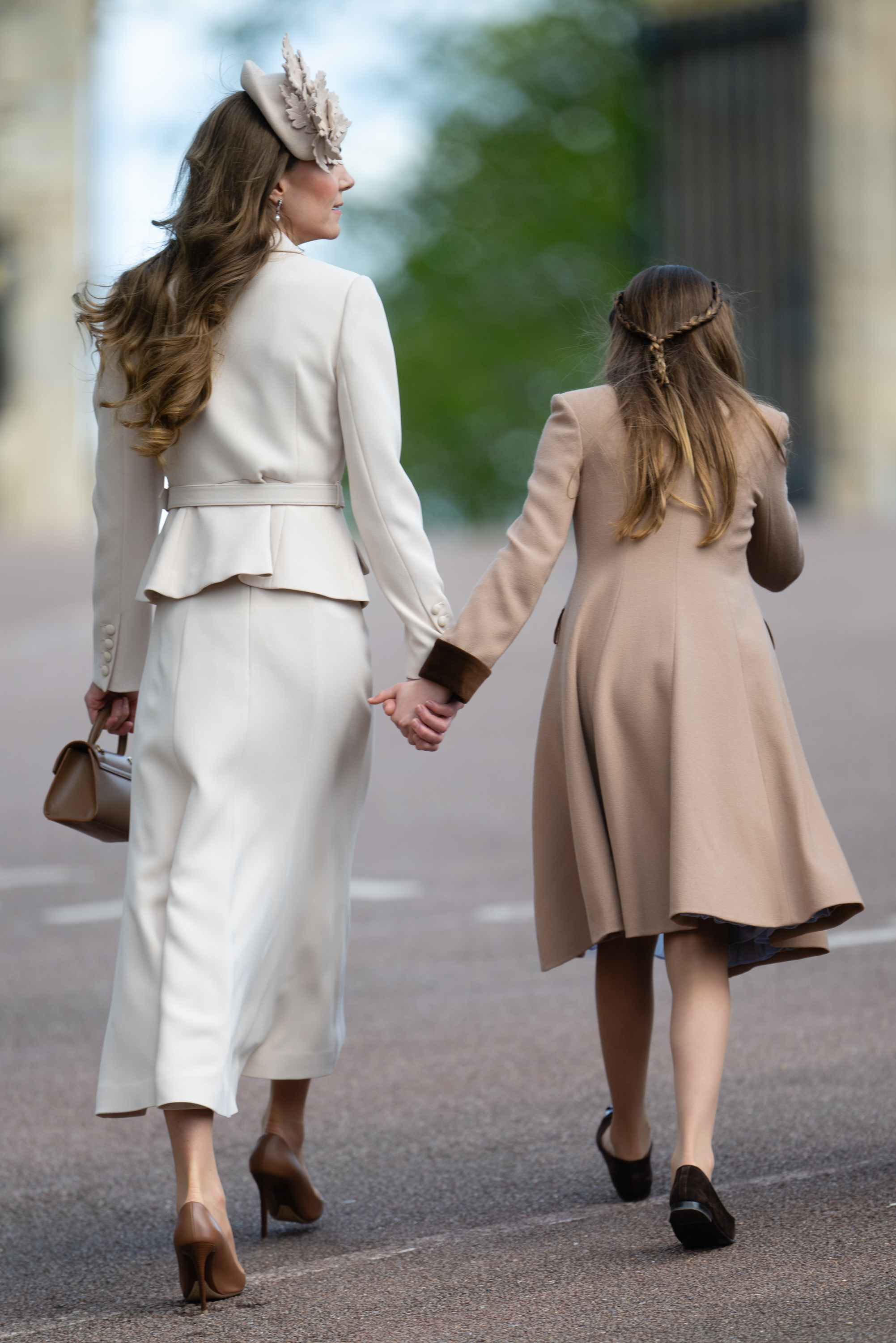 Walking hand in hand towards St George's Chapel on 5 April 2026, the Princess of Wales and Princess Charlotte make their way into the Easter Matins Service at Windsor. Seen from behind, the full detail of the Princess of Wales's cream Self Portrait ensemble comes into view. Princess Charlotte, in her camel coat with brown velvet trim, her hair swept back in a plaited braid, keeps pace alongside her mother.