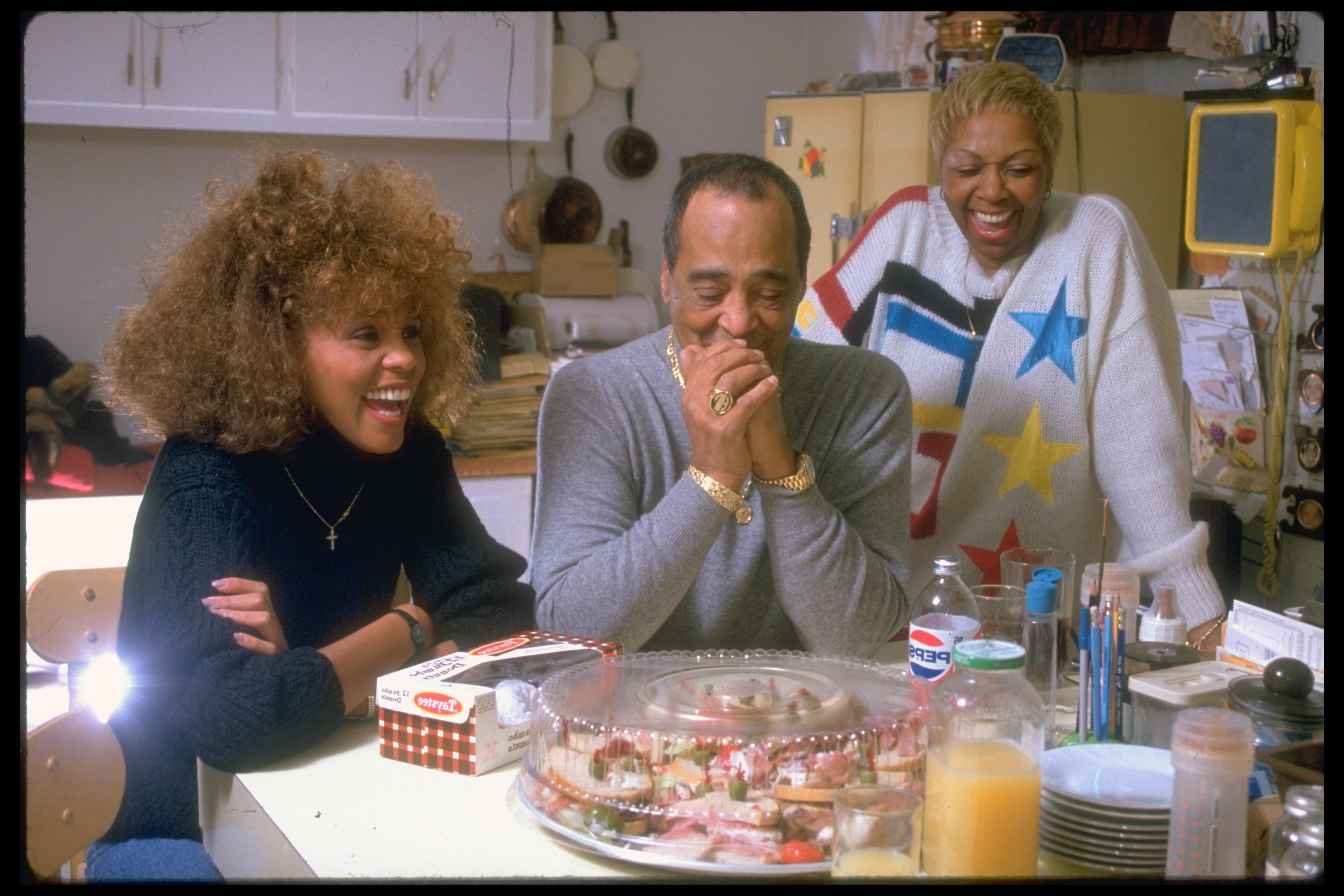 Whitney Houston, annesi Cissy ve babası John ile evde mutfak masasında oturuyor, 01 Ocak 1987 |  Kaynak: Getty Images