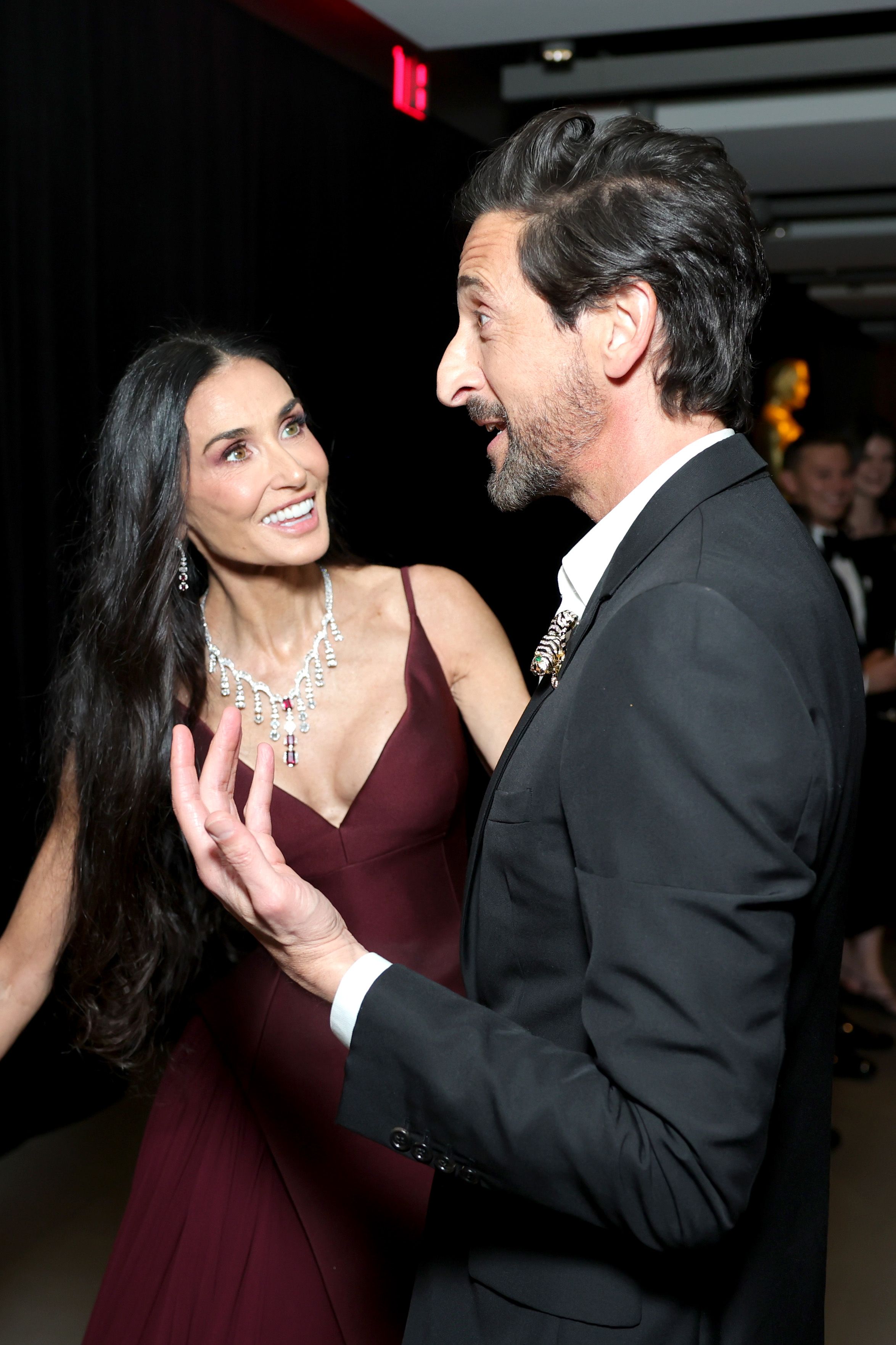Beaming and animated, Demi Moore shares a light-hearted exchange with Adrien Brody, her body language open and expressive as the two actors lean in during a lively moment at the gala.