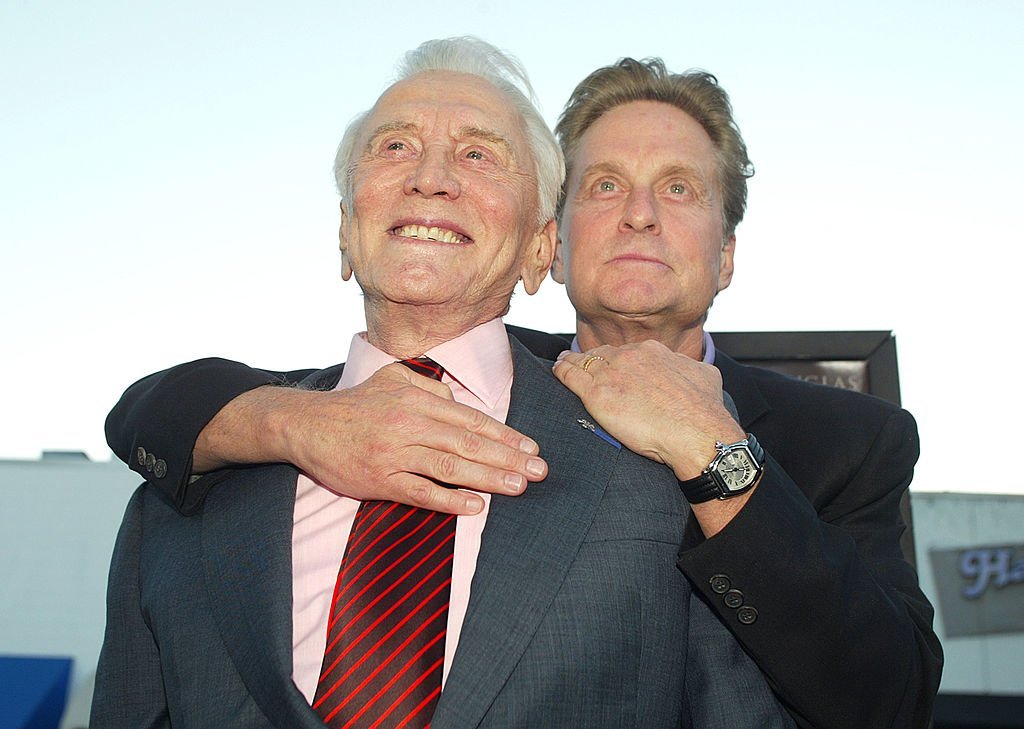 Kirk Douglas stands with son Michael Douglas as he hugs him from behind at the premiere of "It Runs In The Family" on April 7, 2003. | Source: Getty Images