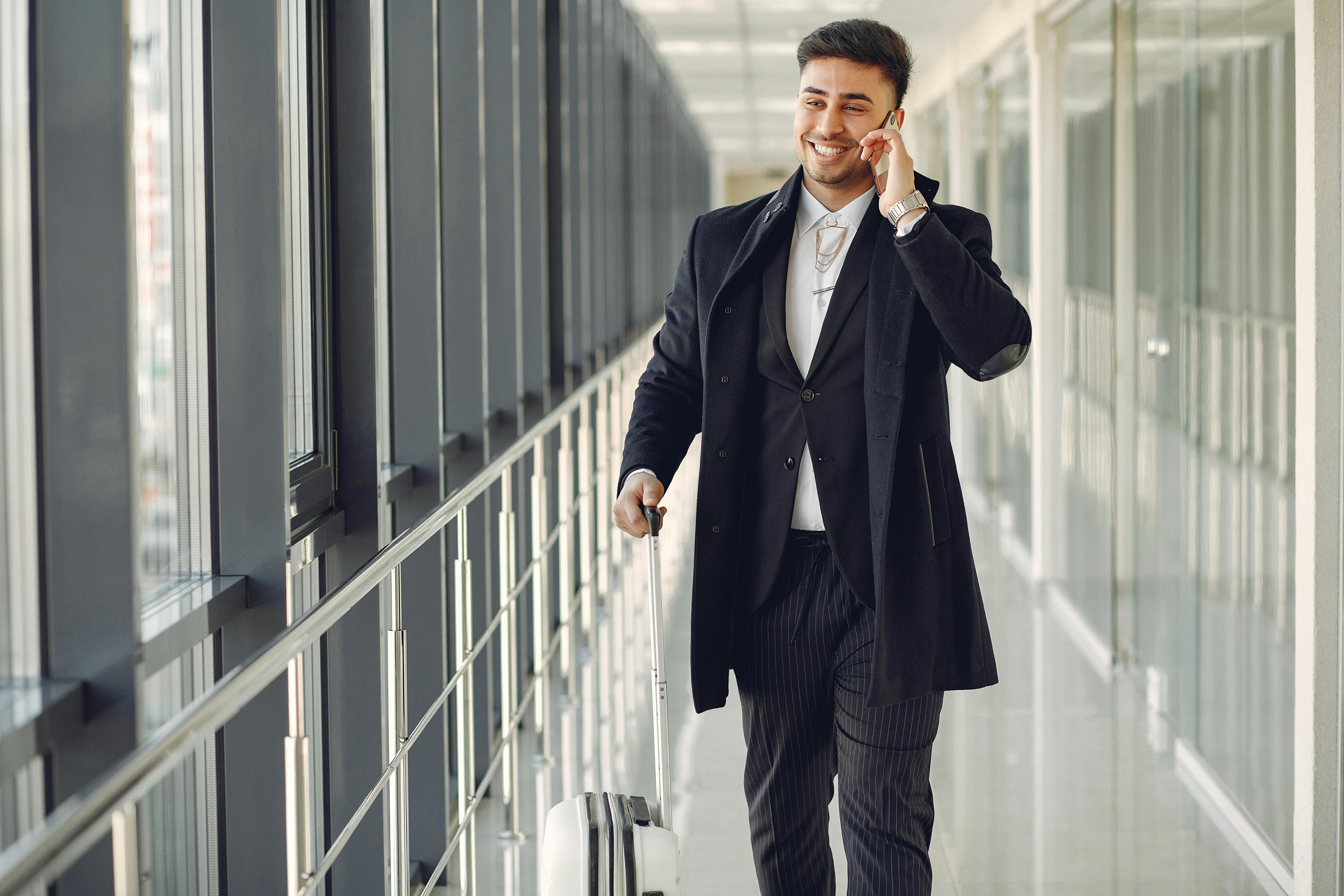 A happy man talking on the phone while walking with his luggage | Source: Pexels