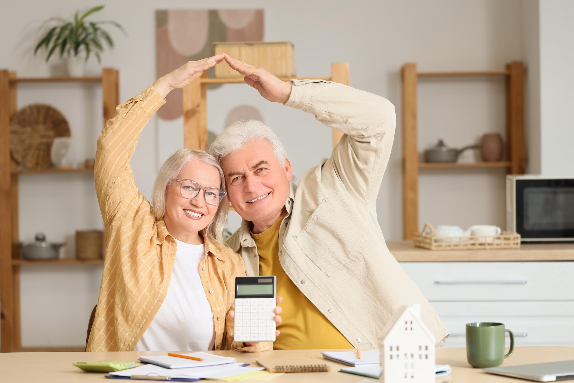 A smiling couple gesturing a roof over their heads while holding a calculator | Source: Shutterstock