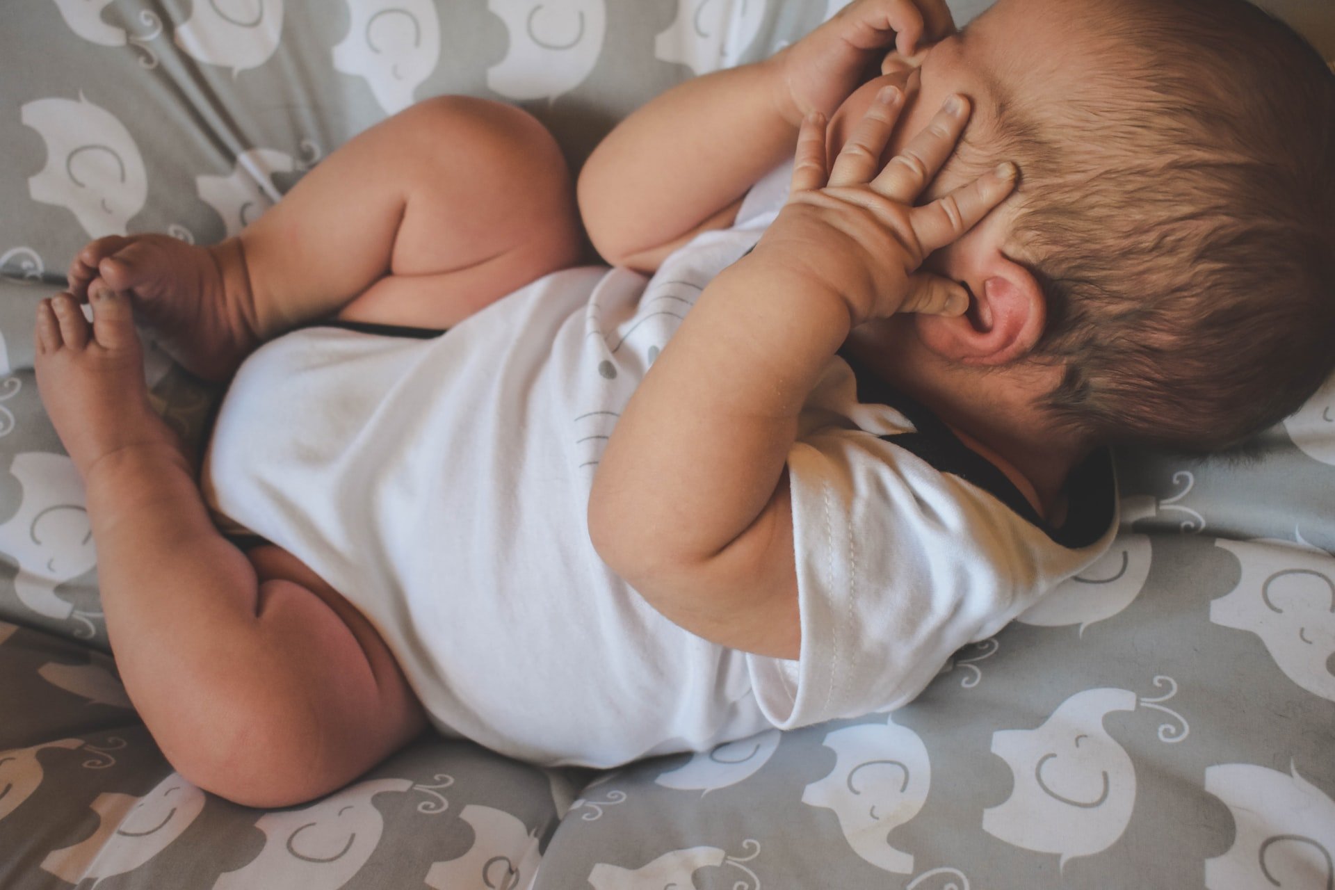 Un bebé en una cama con las manos sobre su rostro. | Foto: Unsplash