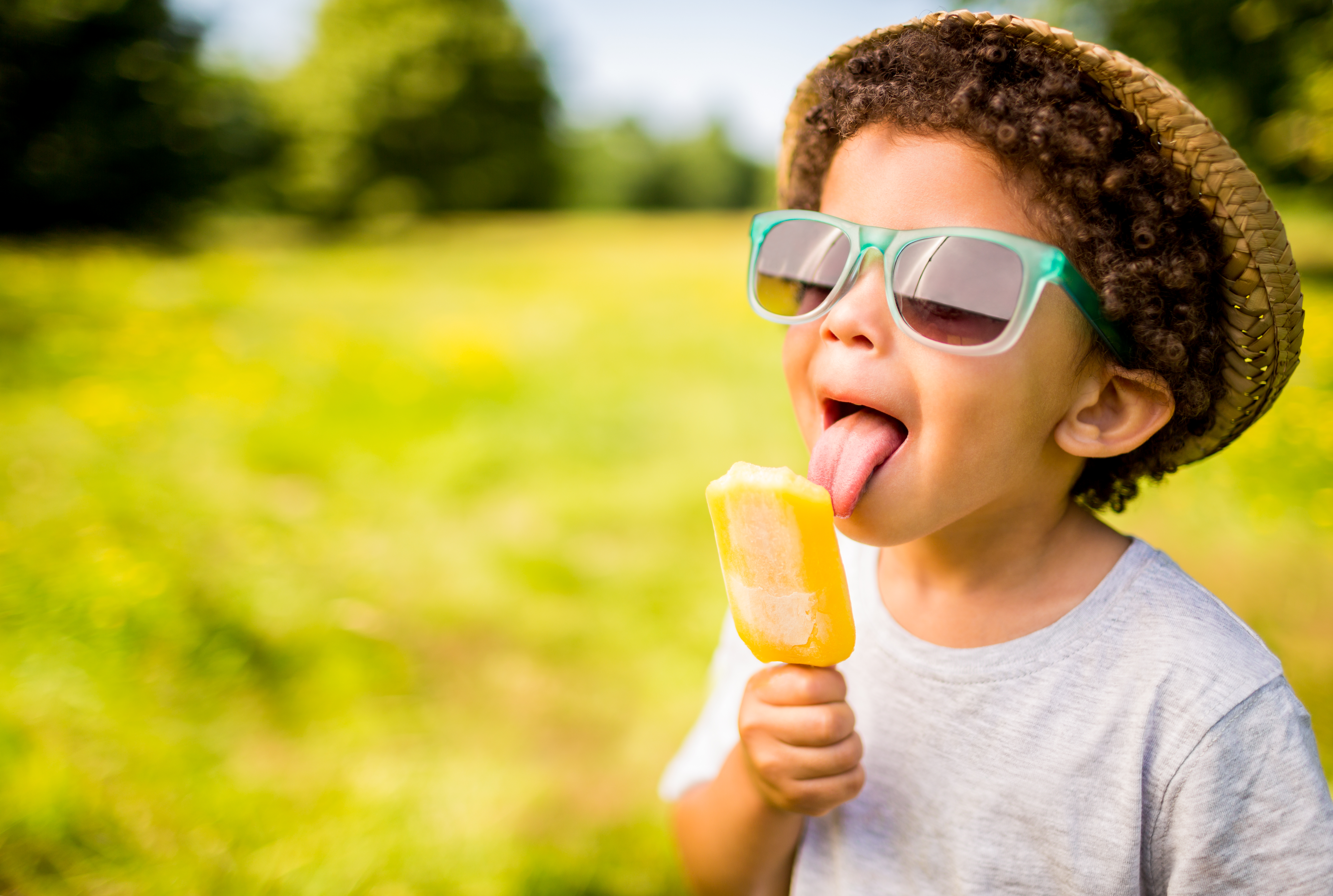 Boy in sunglasses and hat eating popsicle outdoors | Source: Getty Images