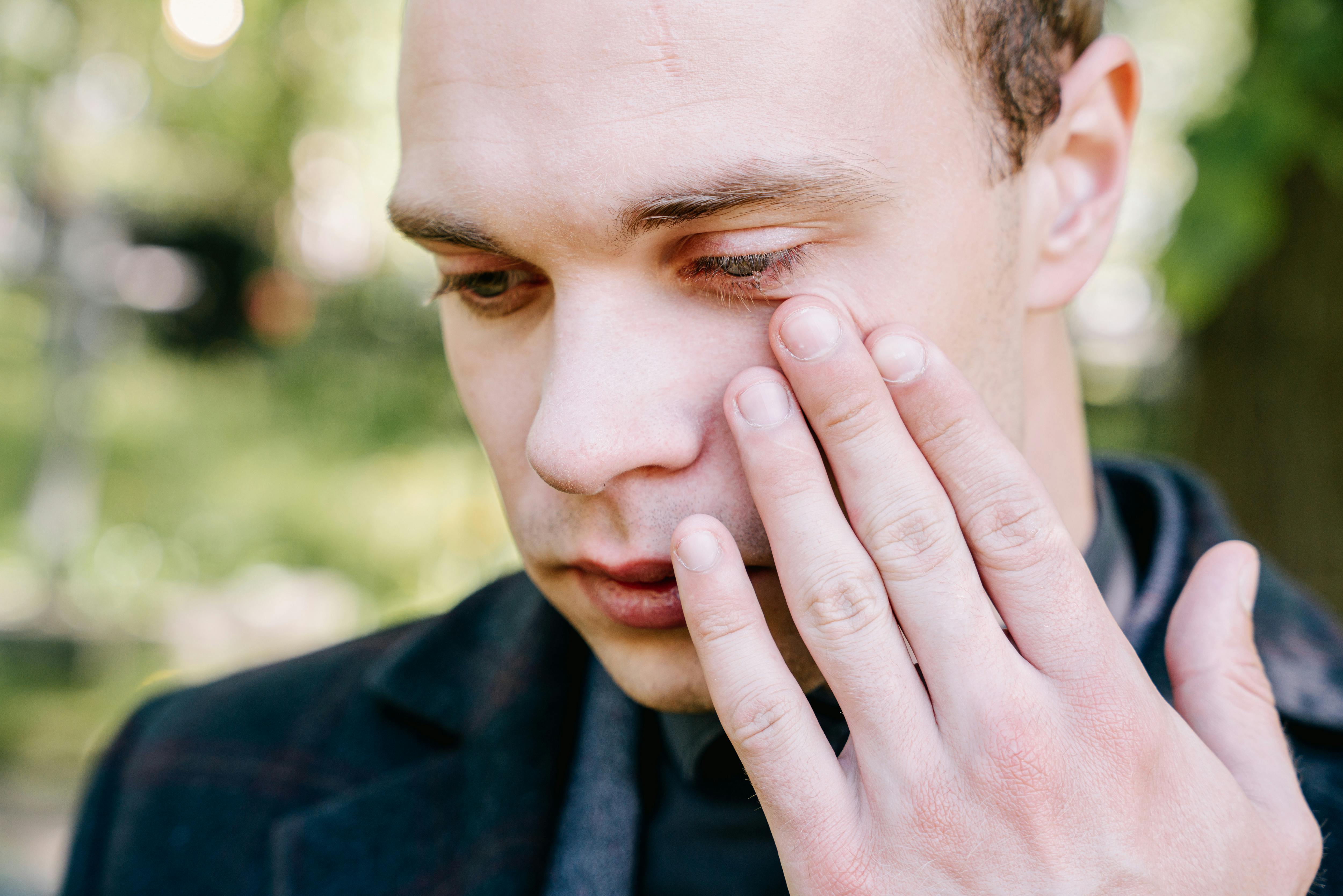A sad young man wiping tears from his eyes | Source: Pexels