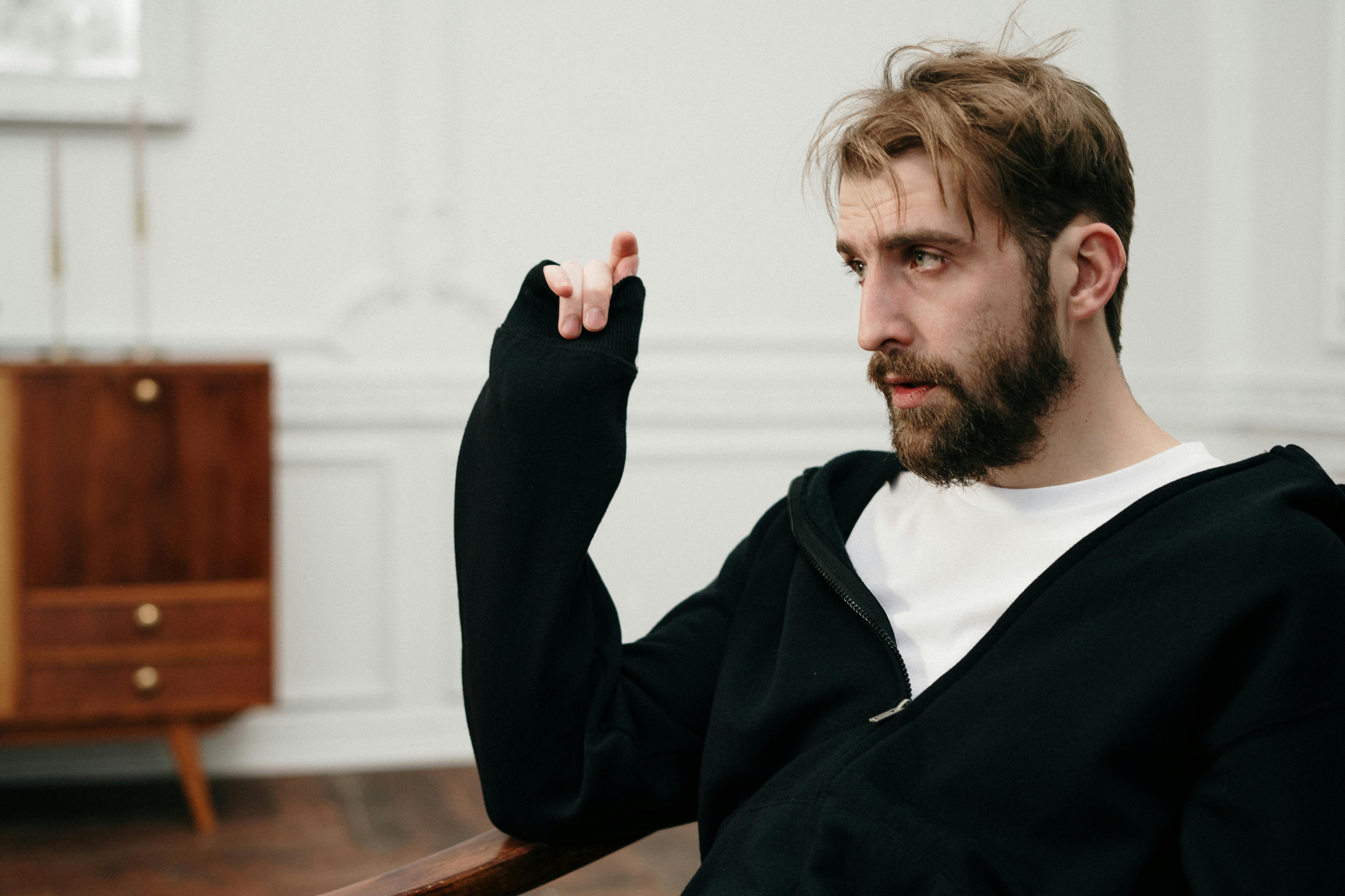 Man siting on a brown wooden chair and resting his right hand on the armrest | Source: Pexels