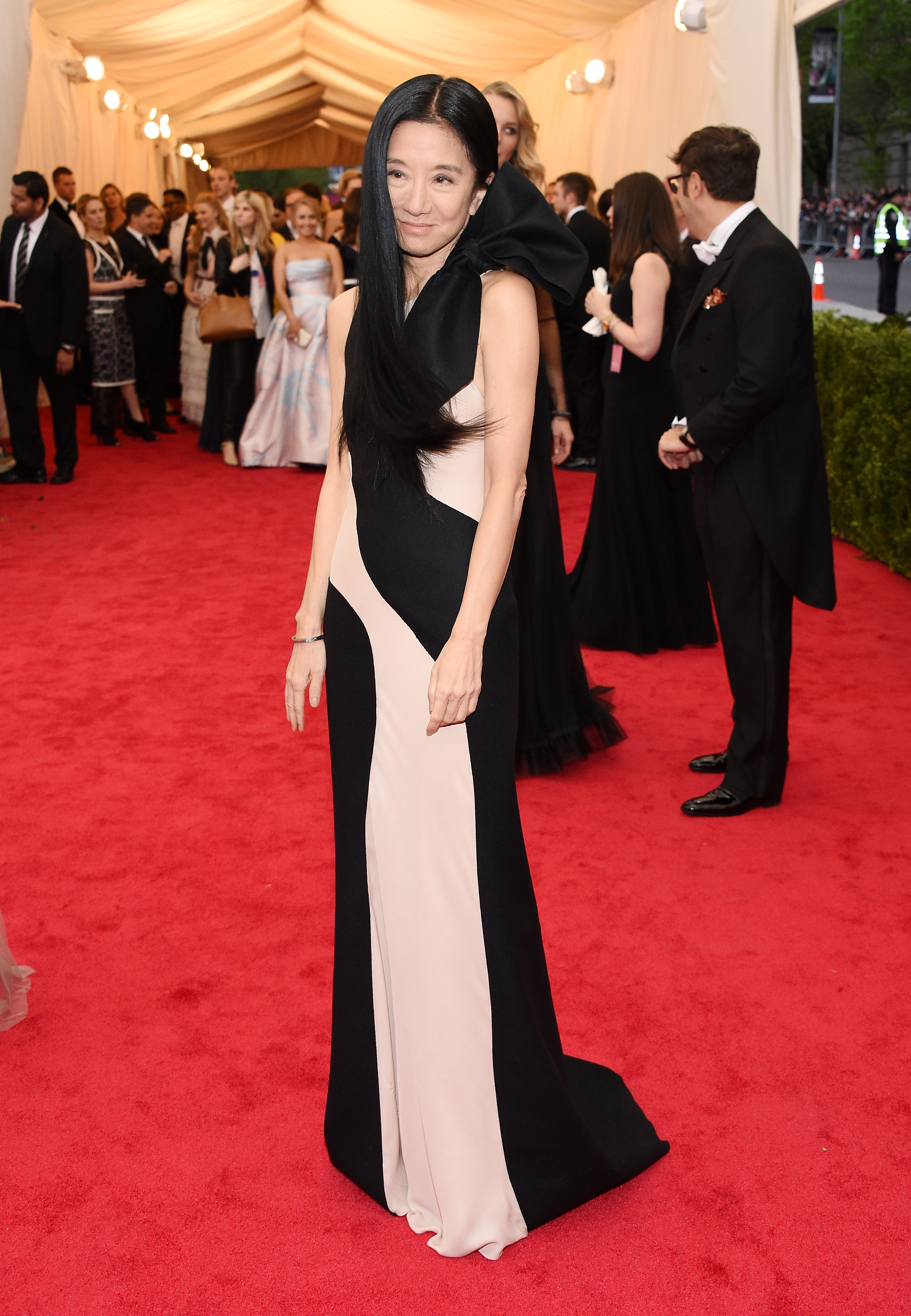 At the Met Gala, Vera Wang stuns in a black-and-cream gown with a bold asymmetrical design. Her sleek hair and subtle makeup complete the elegant look as she walks the red carpet surrounded by onlookers and press.