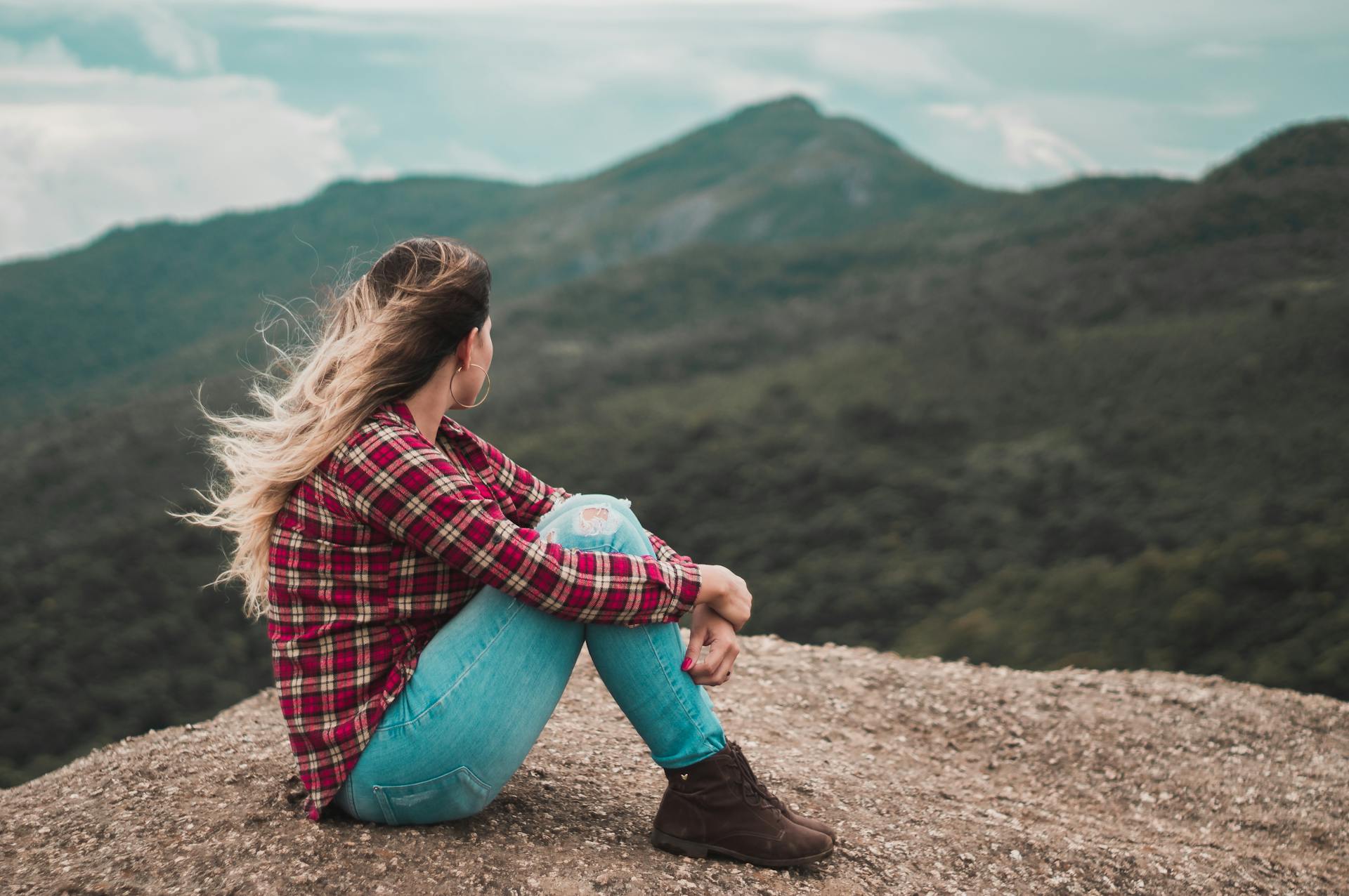 A side view of a woman sitting on the ground overlooking a hill | Source: Pexels