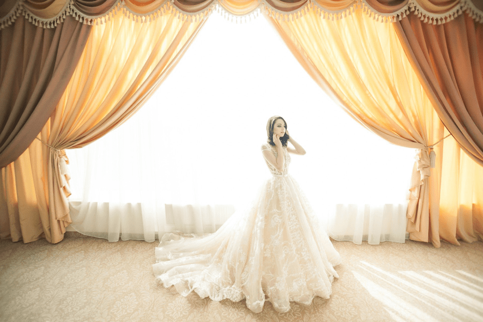 Eine Braut trägt ein Spitzenhochzeitskleid an einem Fenster. | Quelle: Pixabay