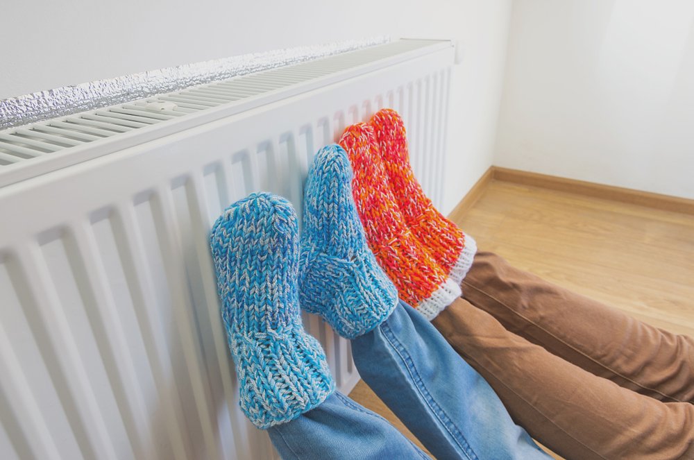 Personas calentando sus pies frente al radiador. | Foto: Shutterstock