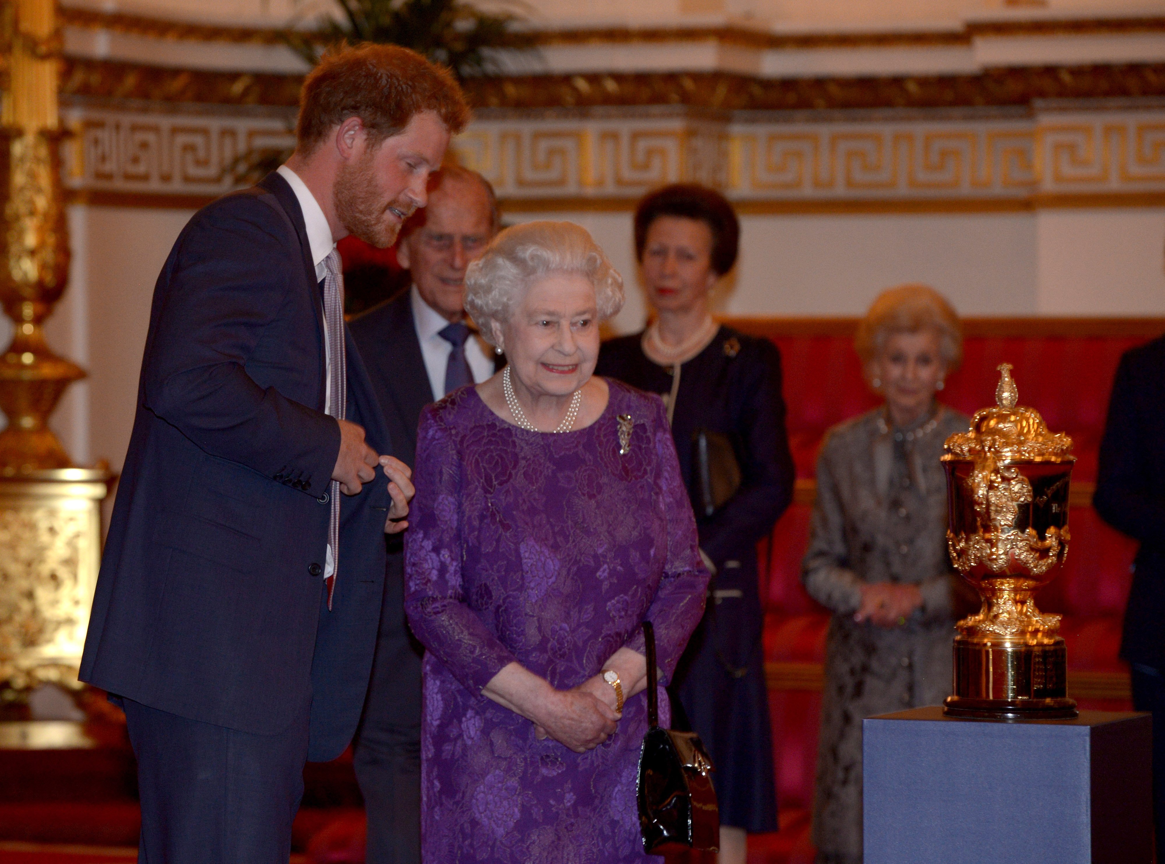 Königin Elizabeth II. und Prinz Harry betrachten den Webb Ellis Cup während eines Empfangs anlässlich der Rugby-Weltmeisterschaft 2015 im Buckingham Palast am 12. Oktober 2015 in London, Vereinigtes Königreich. | Quelle: Getty Images