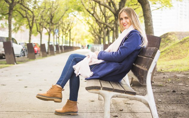 Mujer sentada en un parque usando un abrigo azul. │Foto: Freepik