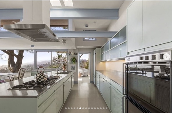 Pale cabinetry and streamlined appliances give the kitchen a clean, understated look, while a long island provides generous preparation and cooking space. Windows positioned around the room bring in views of the hillside and mature trees, continuing the property's strong connection between its indoor and outdoor surroundings. | Source: Instagram/jparkerstanton