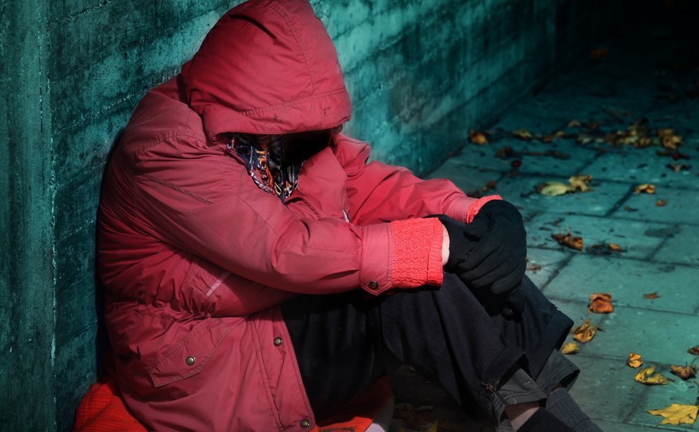 Mujer sin hogar recostada de un muro sentada en el suelo. | Foto: Shutterstock