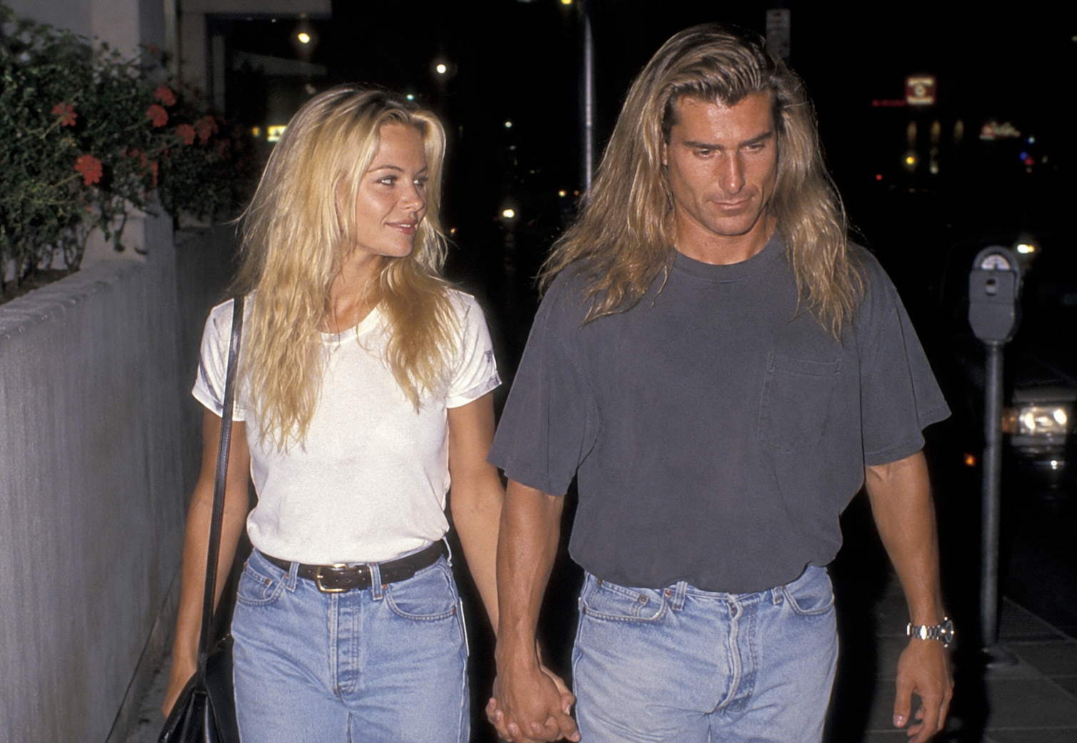 In an AI-generated image, Fabio and Pamela Anderson walk hand in hand at night in casual t-shirts and light-wash jeans, capturing a classic 1990s candid celebrity paparazzi scene. | Source: ChatGPT