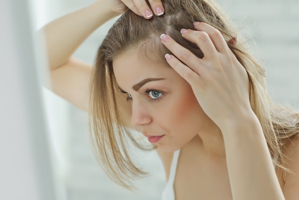 Chica nerviosa mirando en el espejo su cuero cabelludo. Fuente: Shutterstock