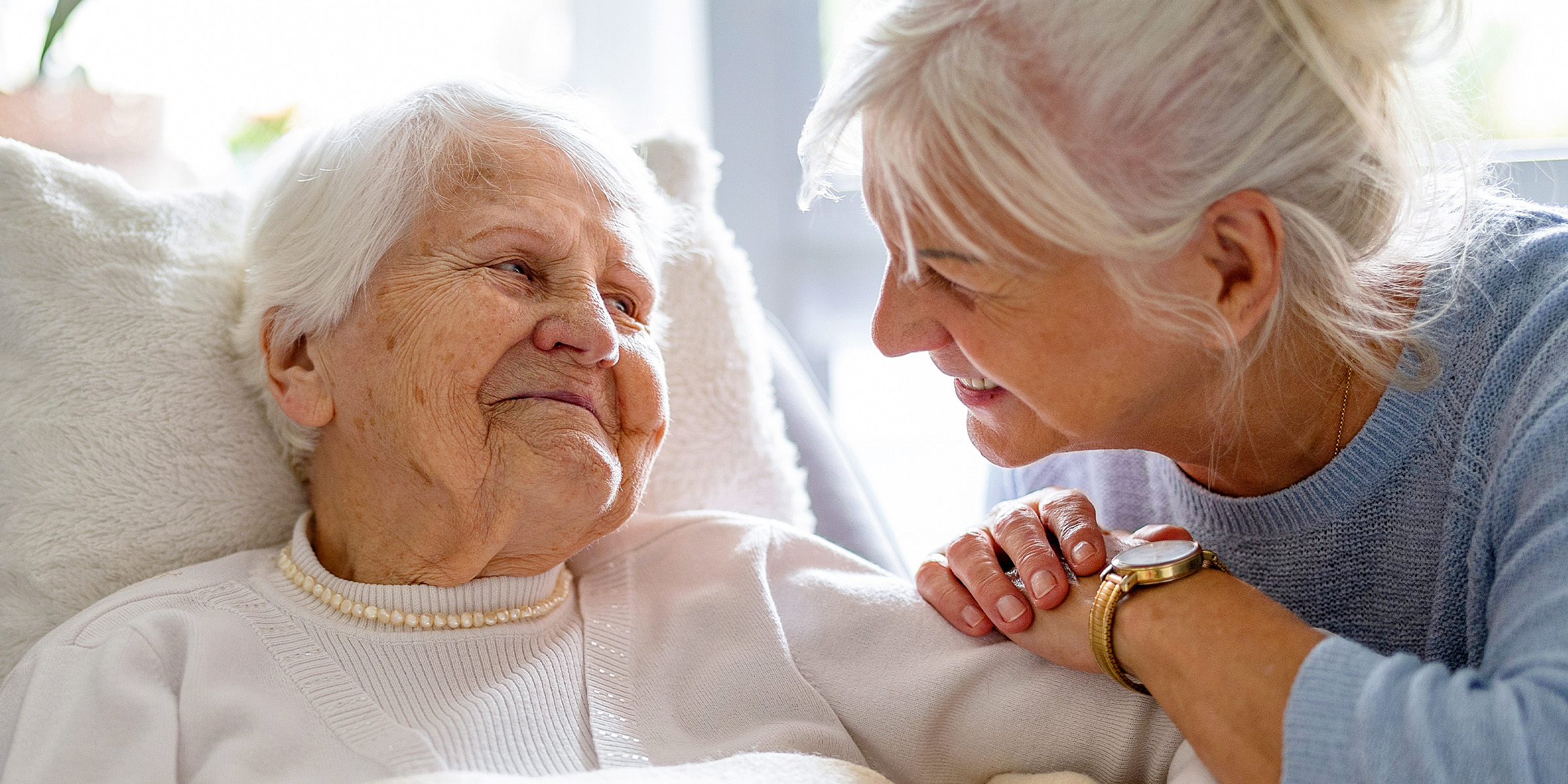 A younger woman sitting and talking to an older one who is lying in bed | Source: Shutterstock