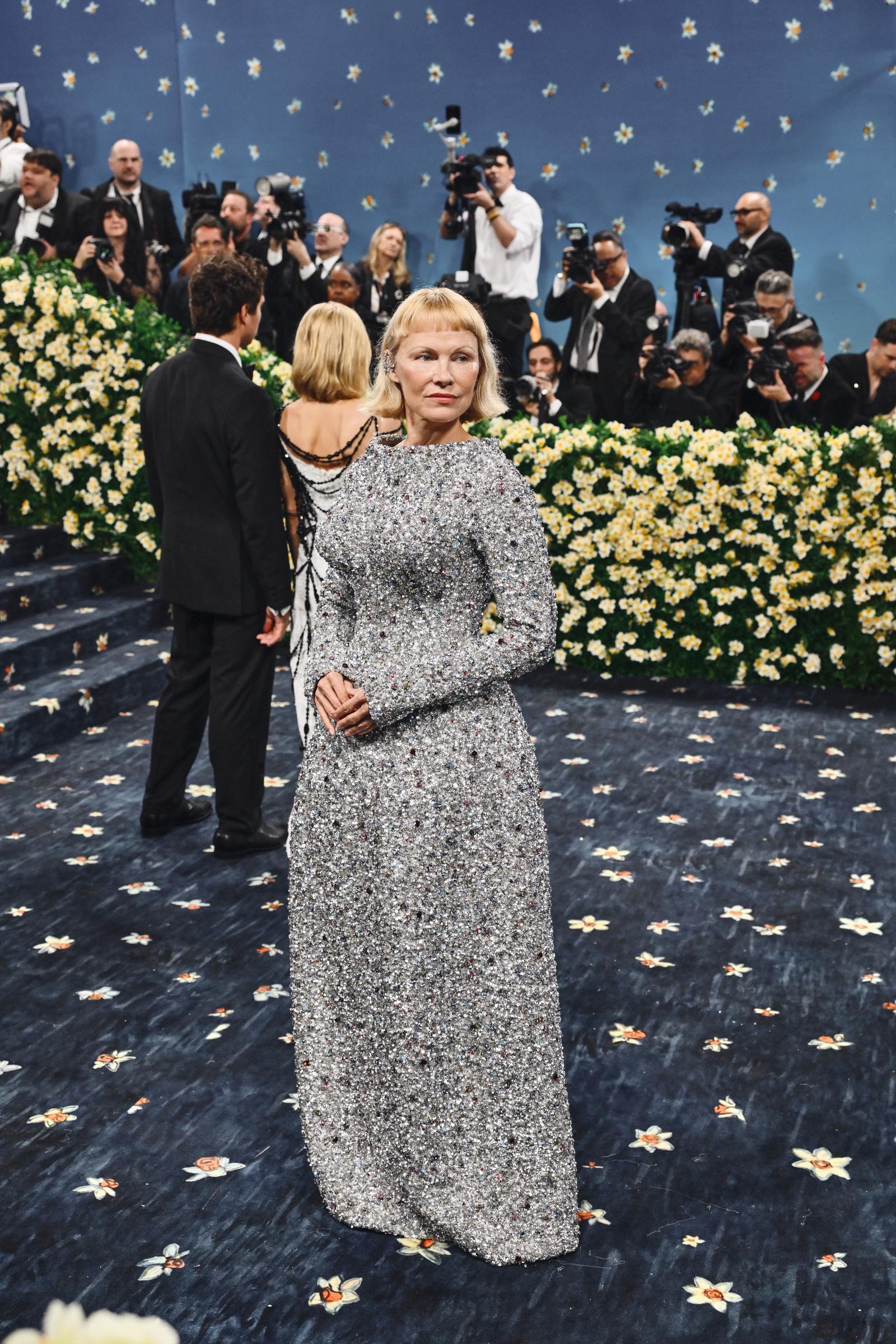 Surrounded by a flurry of photographers, Pamela Anderson stands confidently on the floral Met Gala carpet. Her presence was a nod to quiet elegance, captured during her return to the famed steps of the Metropolitan Museum of Art for the 2025 gala.