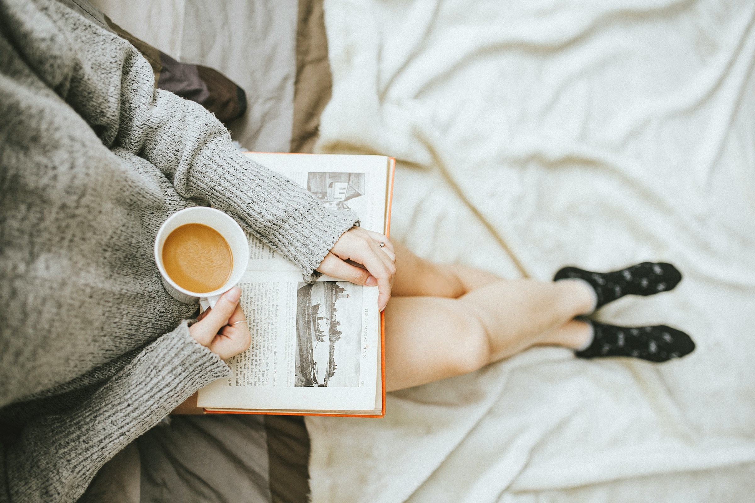 A woman reading a book while enjoying a cup of coffee at home | Source: Unsplash