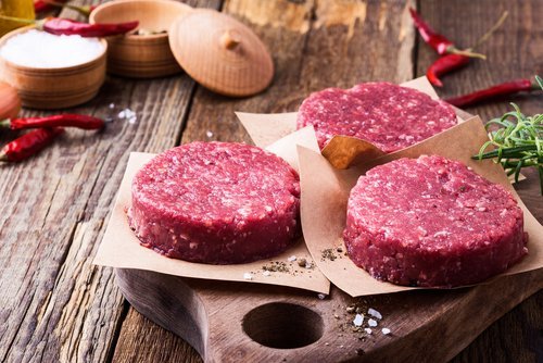 Organic raw ground beef, round patties for making homemade burger on wooden cutting board. | Source: Shutterstock