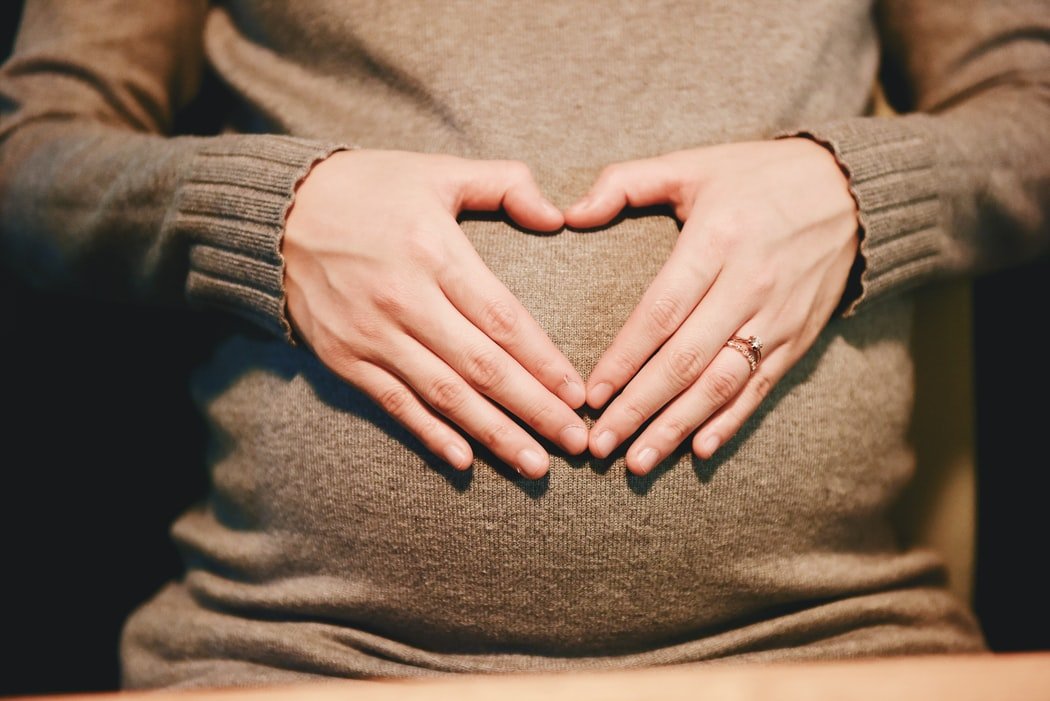 Pregnant woman poses for a portrait while showing the love symbol on her stomach | Photo: Unsplash