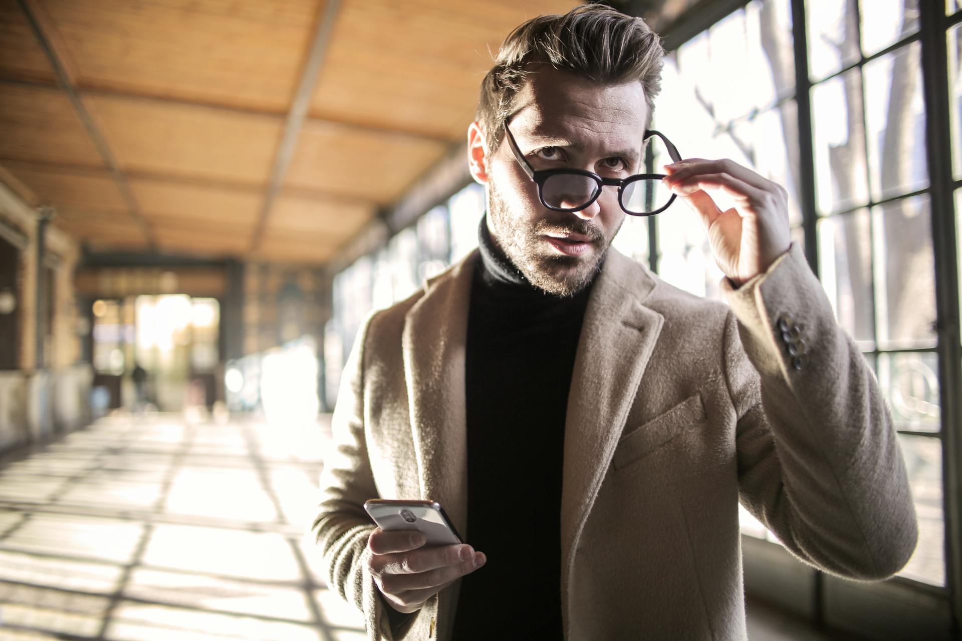 A man holds a phone in one hand and his glasses in the other | Source: Pexels