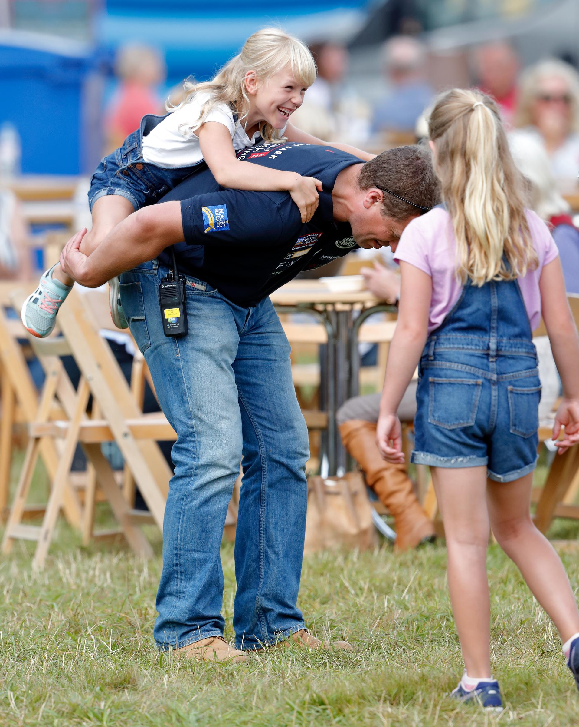 Savannah Phillips (r) looks on as Peter Phillips gives daughter Isla Phillips a piggyback on day 1 of the 2019 Festival of British Eventing at Gatcombe Park on August 2, 2019 in Stroud, England | Source: Getty Images