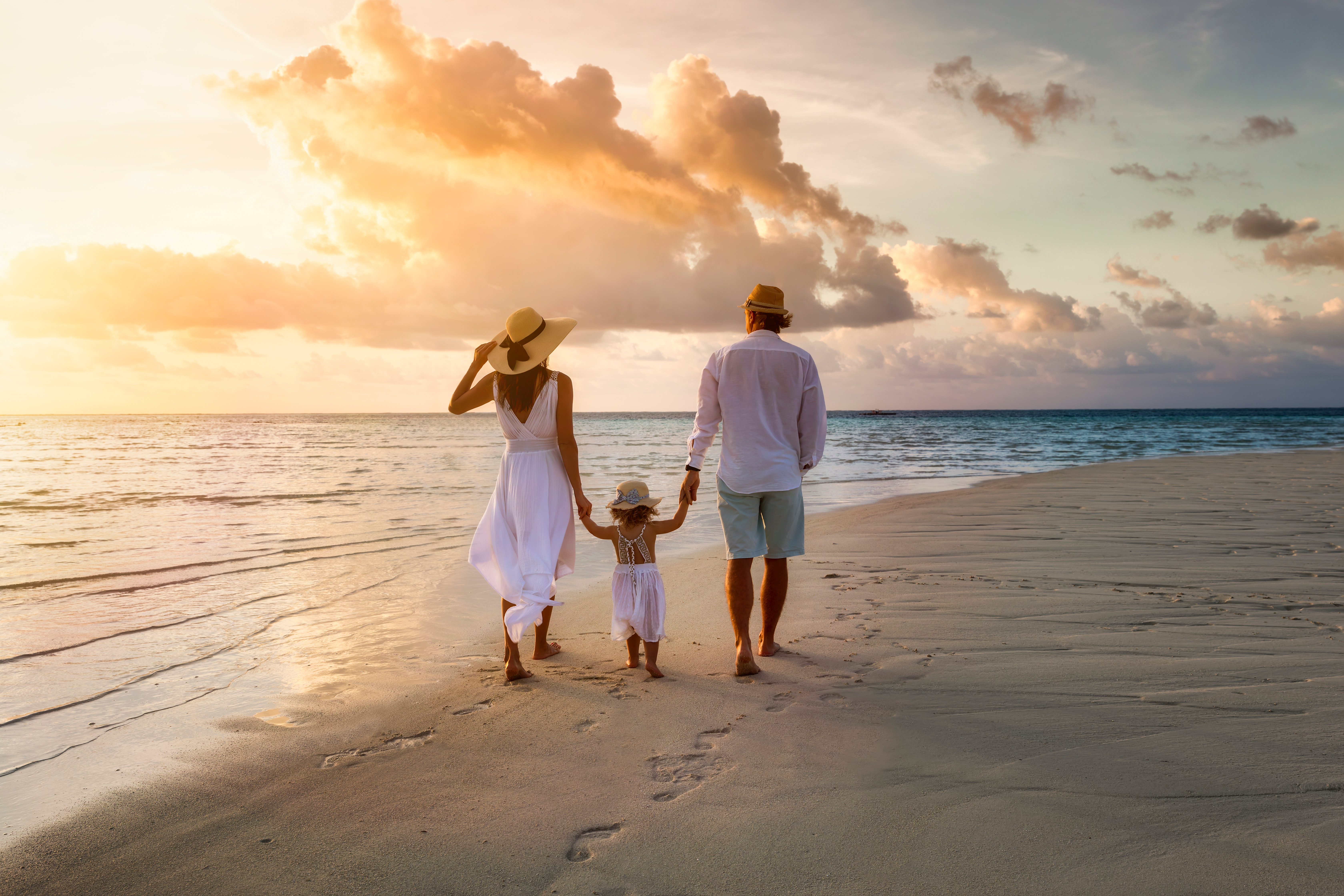 A stylish family dressed in summer white walking hand in hand on a tropical paradise beach during sunset | Source: Shutterstock