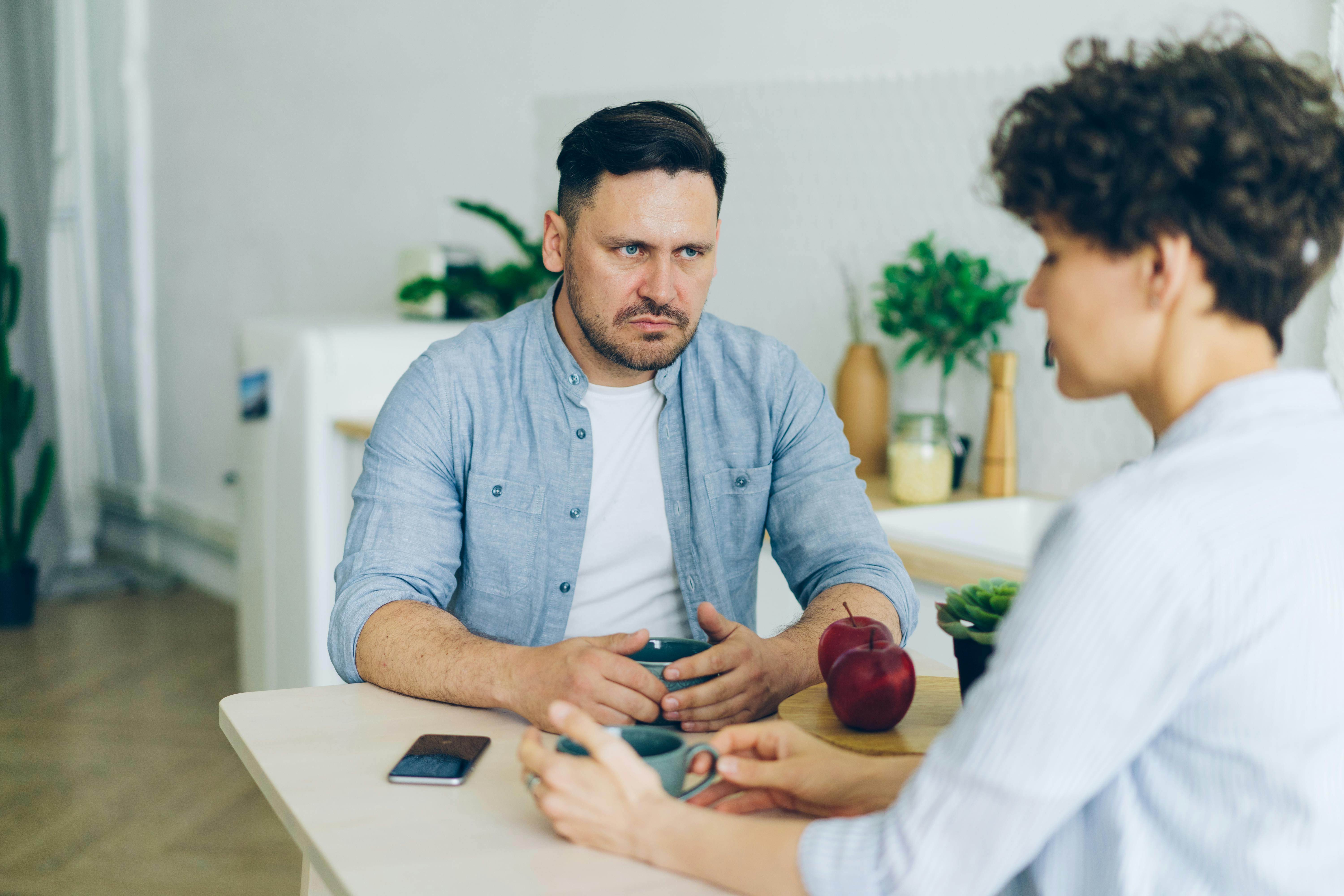 An angry man sitting by the table while looking at a woman | Source: Pexels