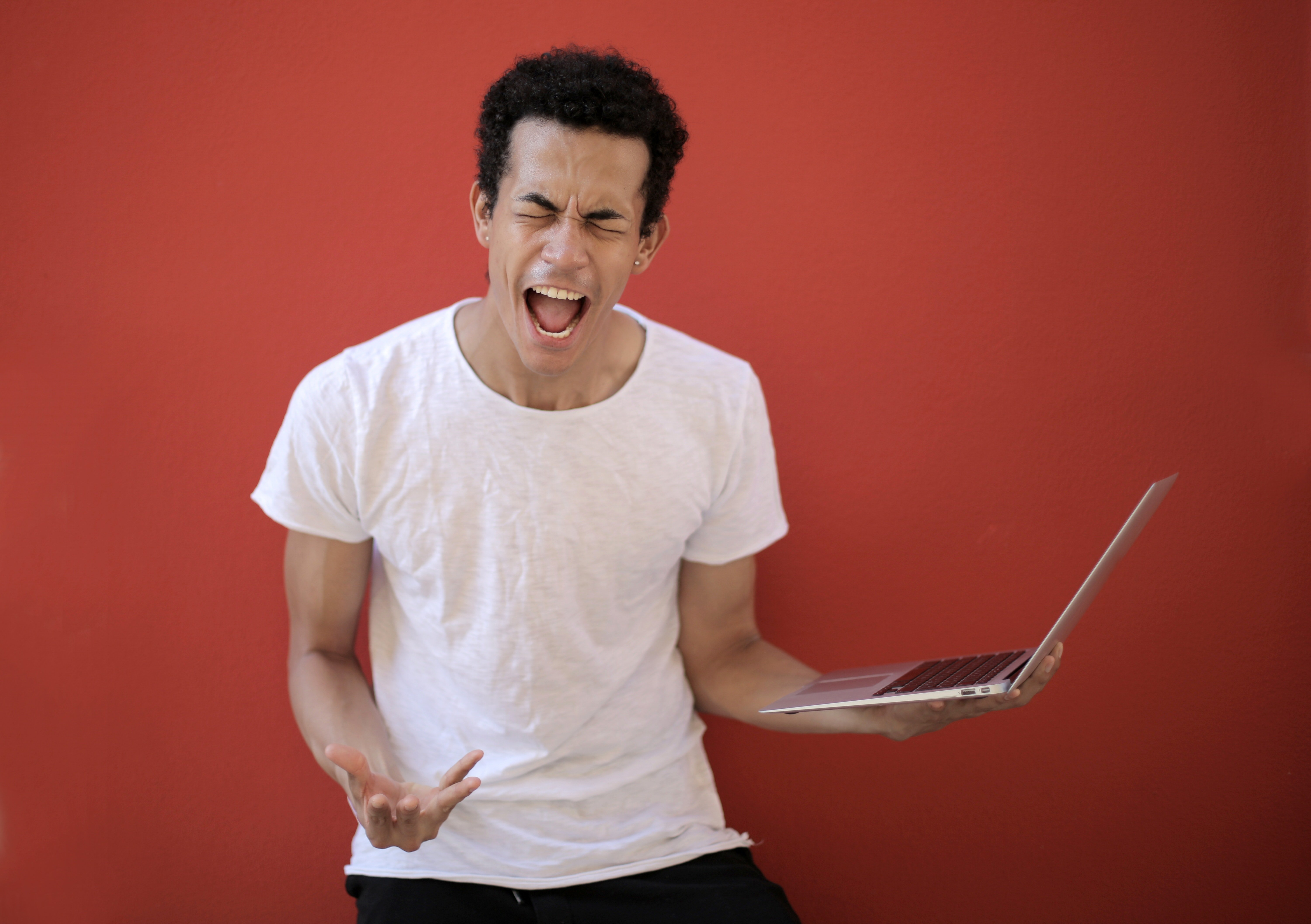 Joven enfurecido con una computadora en su mano. | Foto: Pexels