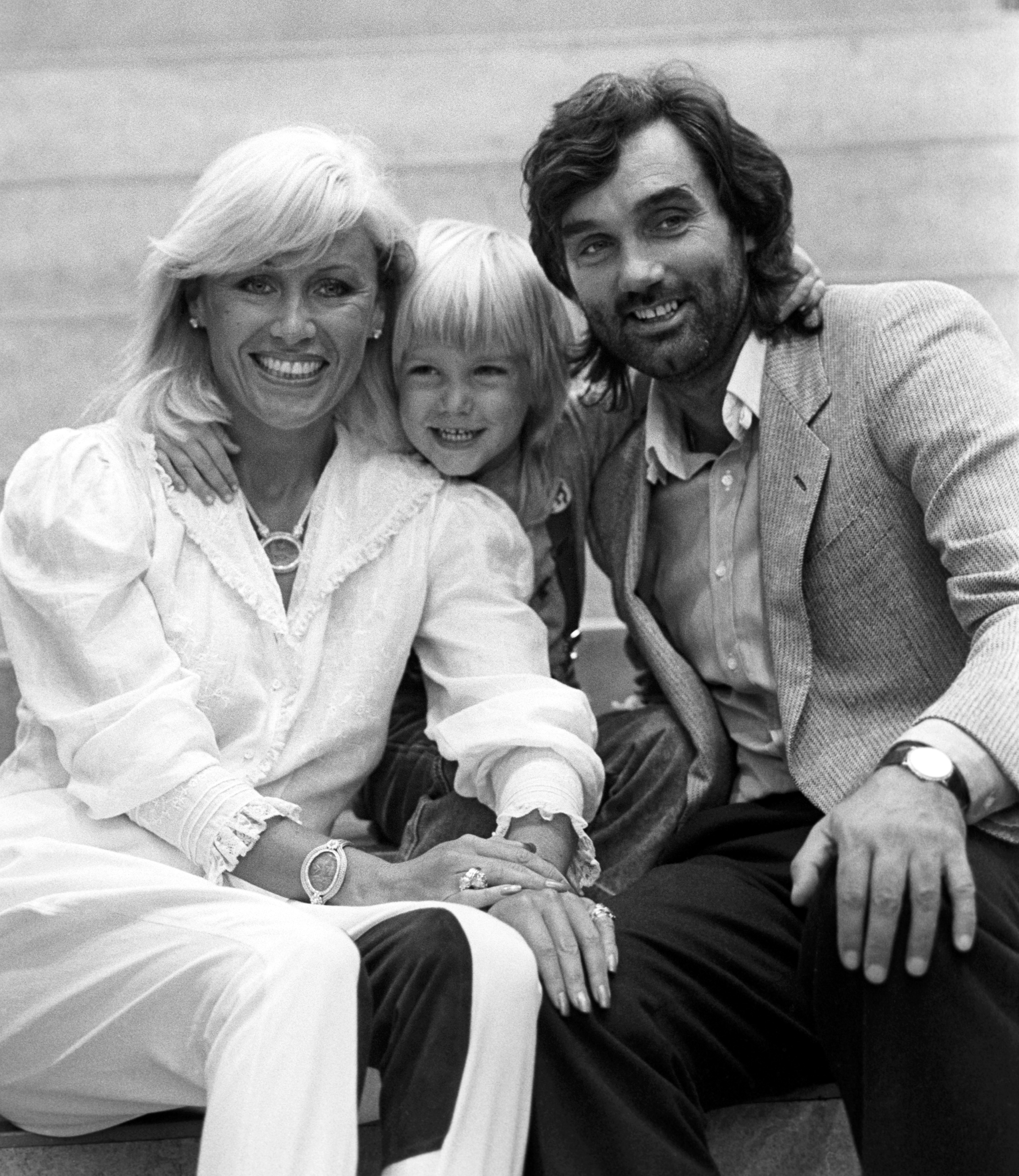 Angie Best is pictured with George Best and their young son Calum, the three sitting closely together and smiling in a warm family moment captured during their earlier years.