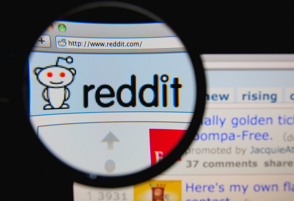 Foto de la página de inicio de Reddit en una pantalla de monitor a través de una lupa. | Fuente: Shutterstock. Foto de la página de inicio de Reddit en una pantalla de monitor a través de una lupa. | Fuente: Shutterstock.