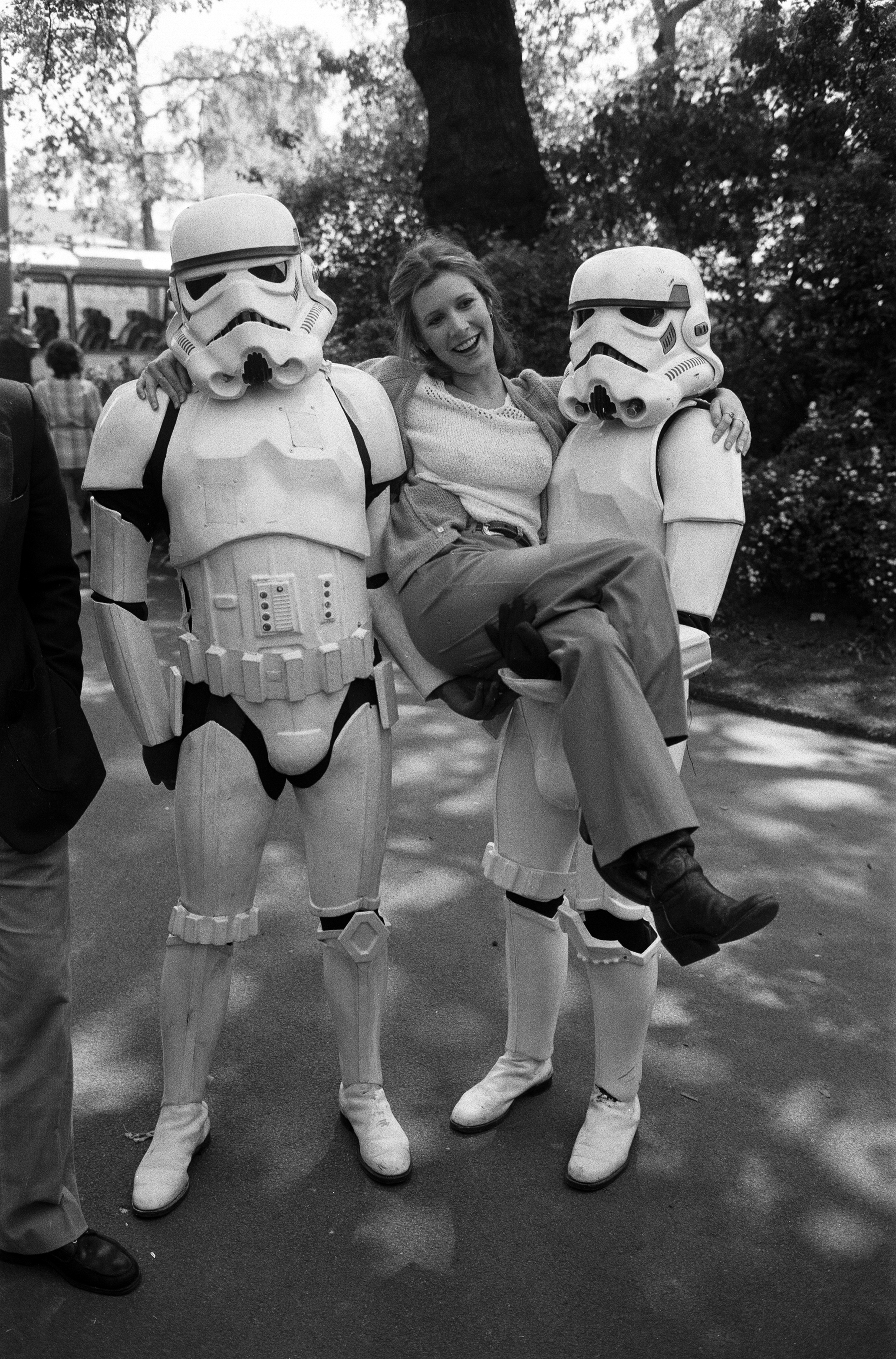 Carrie Fisher und zwei "Star Wars"-Sturmtruppen, die sie während eines Fototermins 1980 an beiden Seiten hochhalten | Quelle: Getty Images