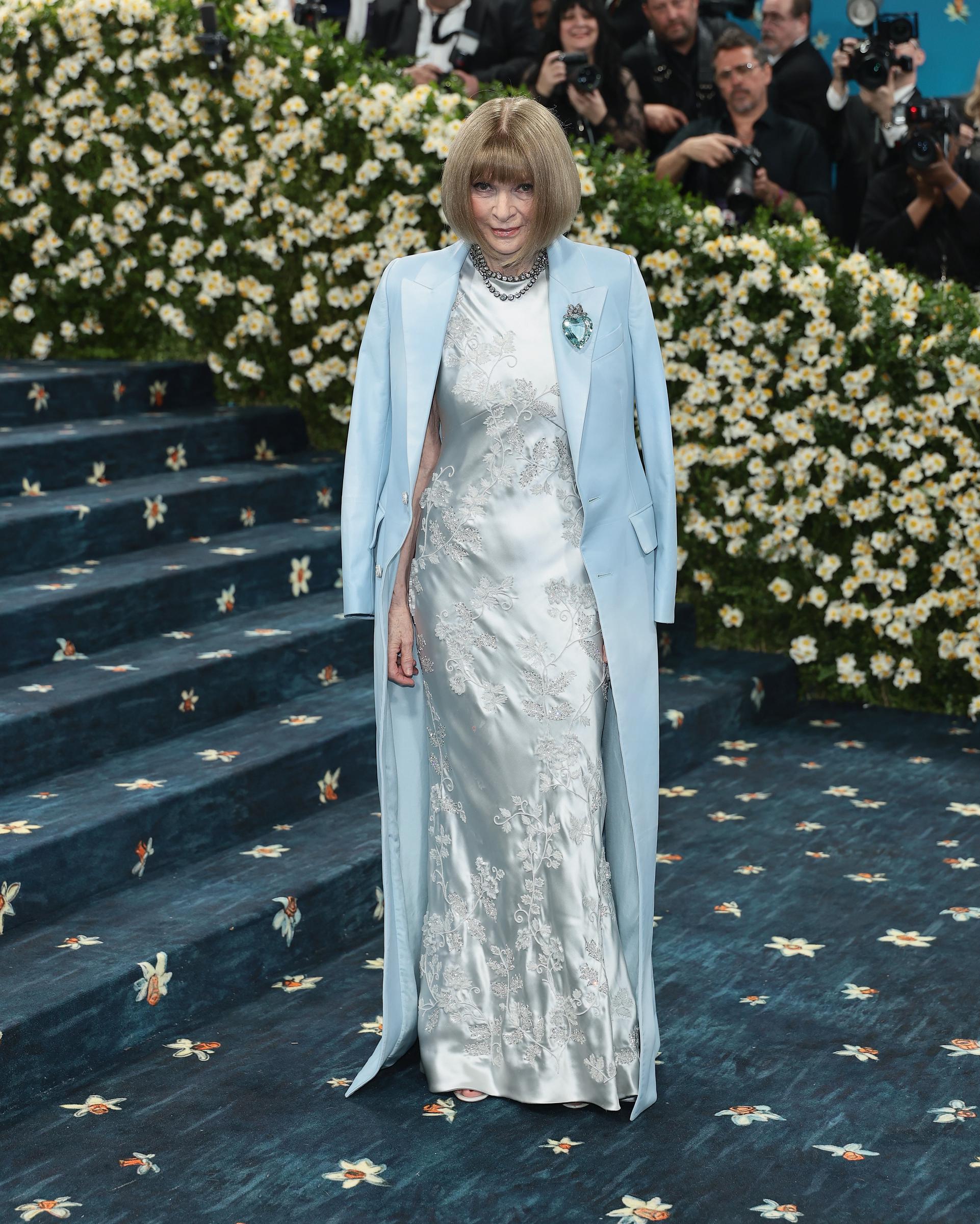 Anna Wintour poses on the Met Gala steps in a powder blue coat draped over an embroidered blue gown, attending the 2025 Met Gala celebrating "Superfine: Tailoring Black Style" at the Metropolitan Museum of Art in New York City.