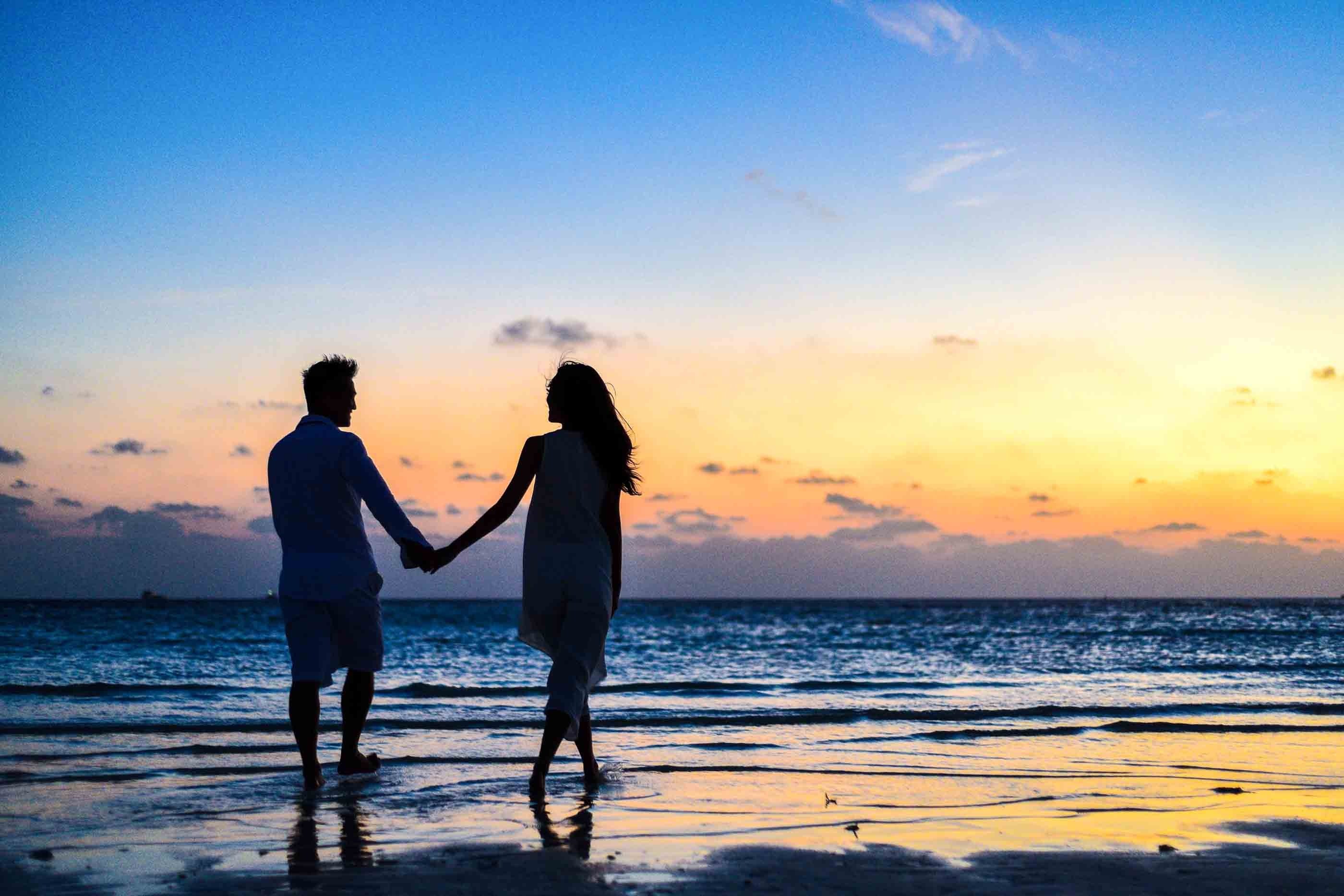 A man and a woman holding hands on seashore during sunrise. | Photo: Pexels 
