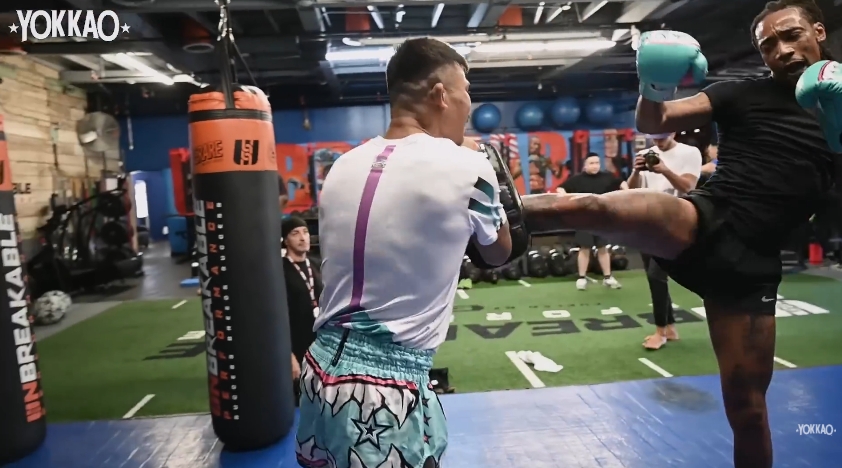 Wiz Khalifa throws a kick while Superlek Kiatmoo9 holds pads during the Muay Thai session. | Source: YouTube/YOKKAO