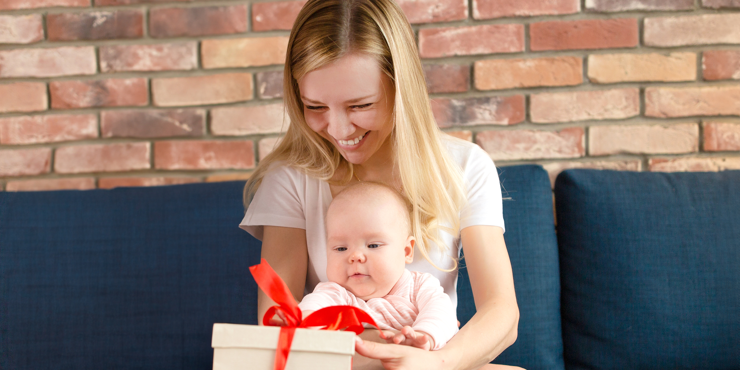 A smiling woman holding a baby and a gift box | Source: Shutterstock