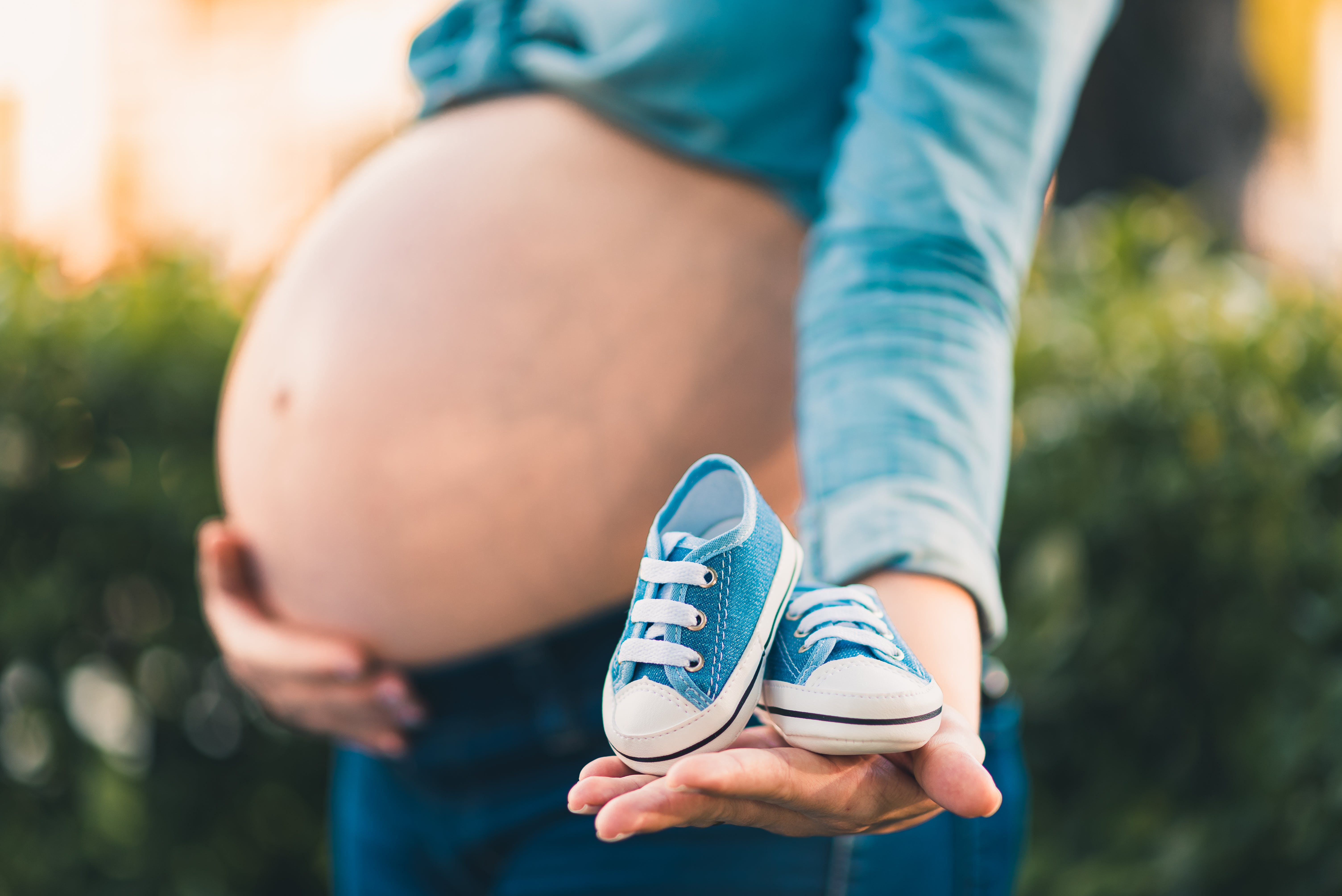 A pregnant woman holding her belly in one hand and a pair of blue baby sneakers in the other | Source: Pexels