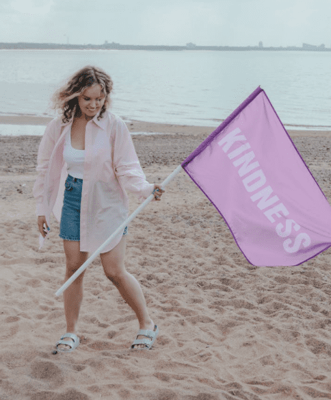 A woman holds up a purple flag that promotes a message of kindness | Pexels/Ron Lach