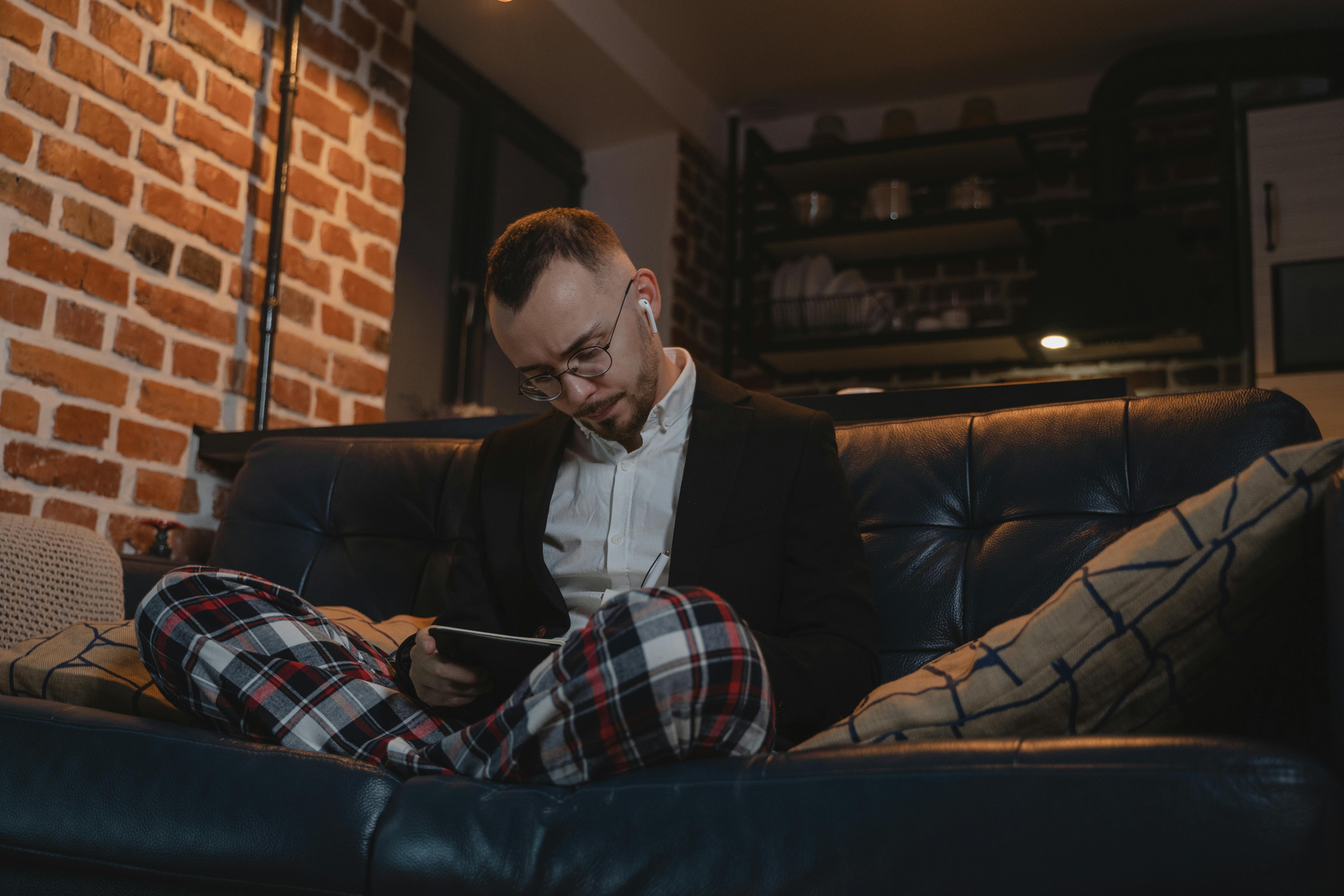 A man dressed in pajama pants and a jacket sitting on a couch | Source: Pexels