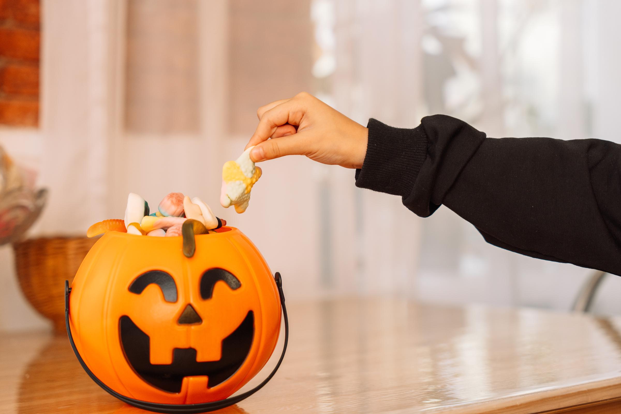 A kid grabbing a gummy from a pumpkin bucket | Source: Getty Images