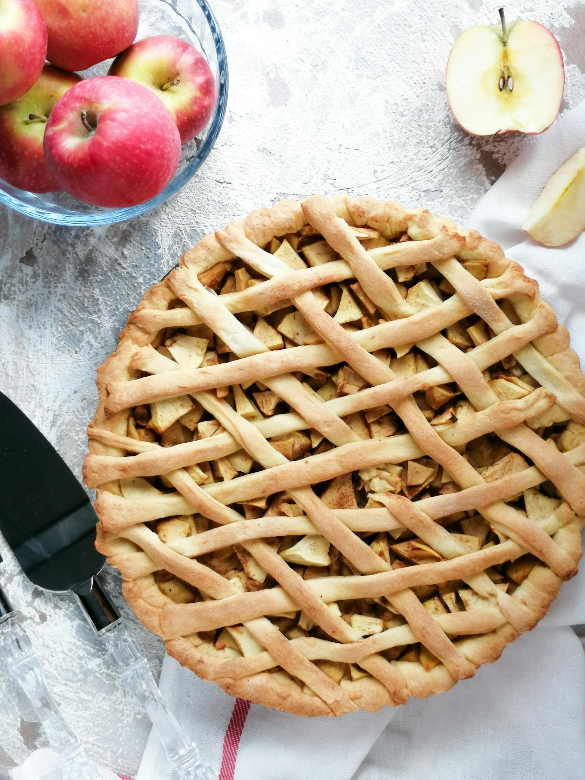 An apple pie lying on a table with a bowl of apples | Source: Pexels