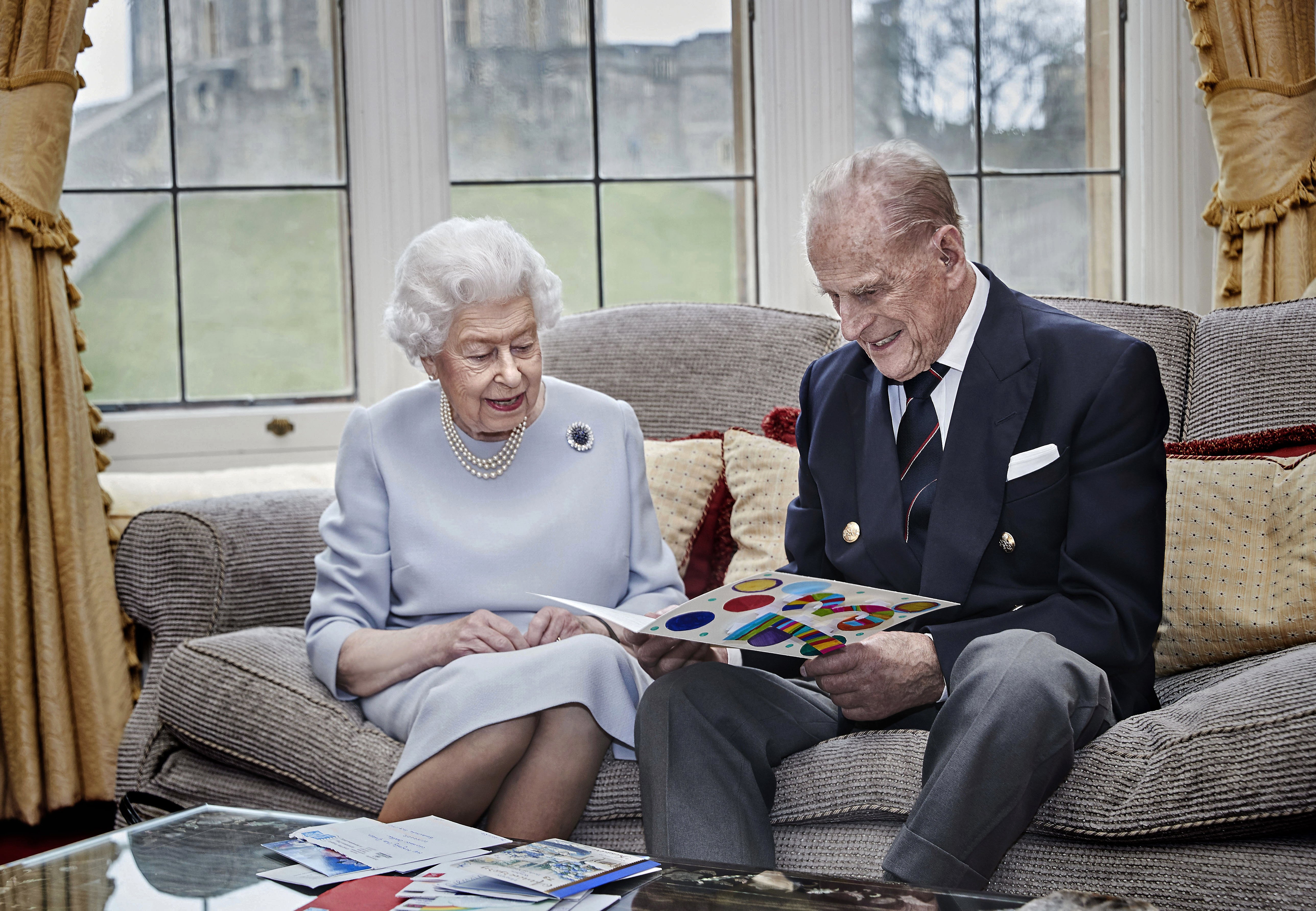 Queen Elizabeth and Prince Philip look at their homemade wedding anniversary card, given to them by their great grandchildren | Photo: Getty Images