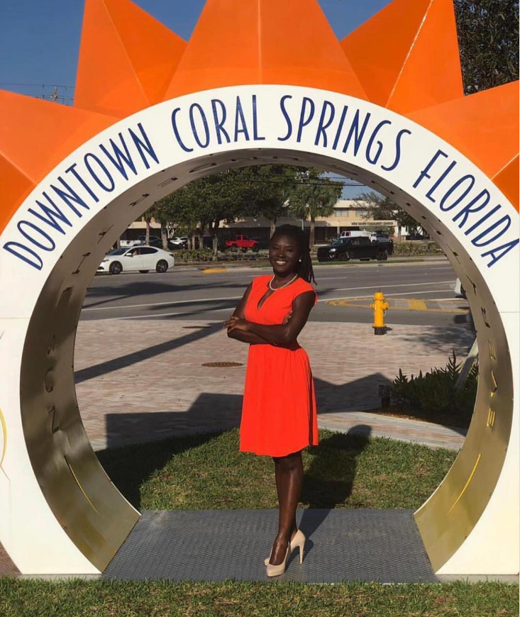 Standing confidently beneath the “Downtown Coral Springs Florida” arch, Nancy Metayer Bowen poses in a vibrant red dress with arms crossed, her bright smile matching the sunny, civic backdrop. | Source: Instagram/nancymetayerbowen