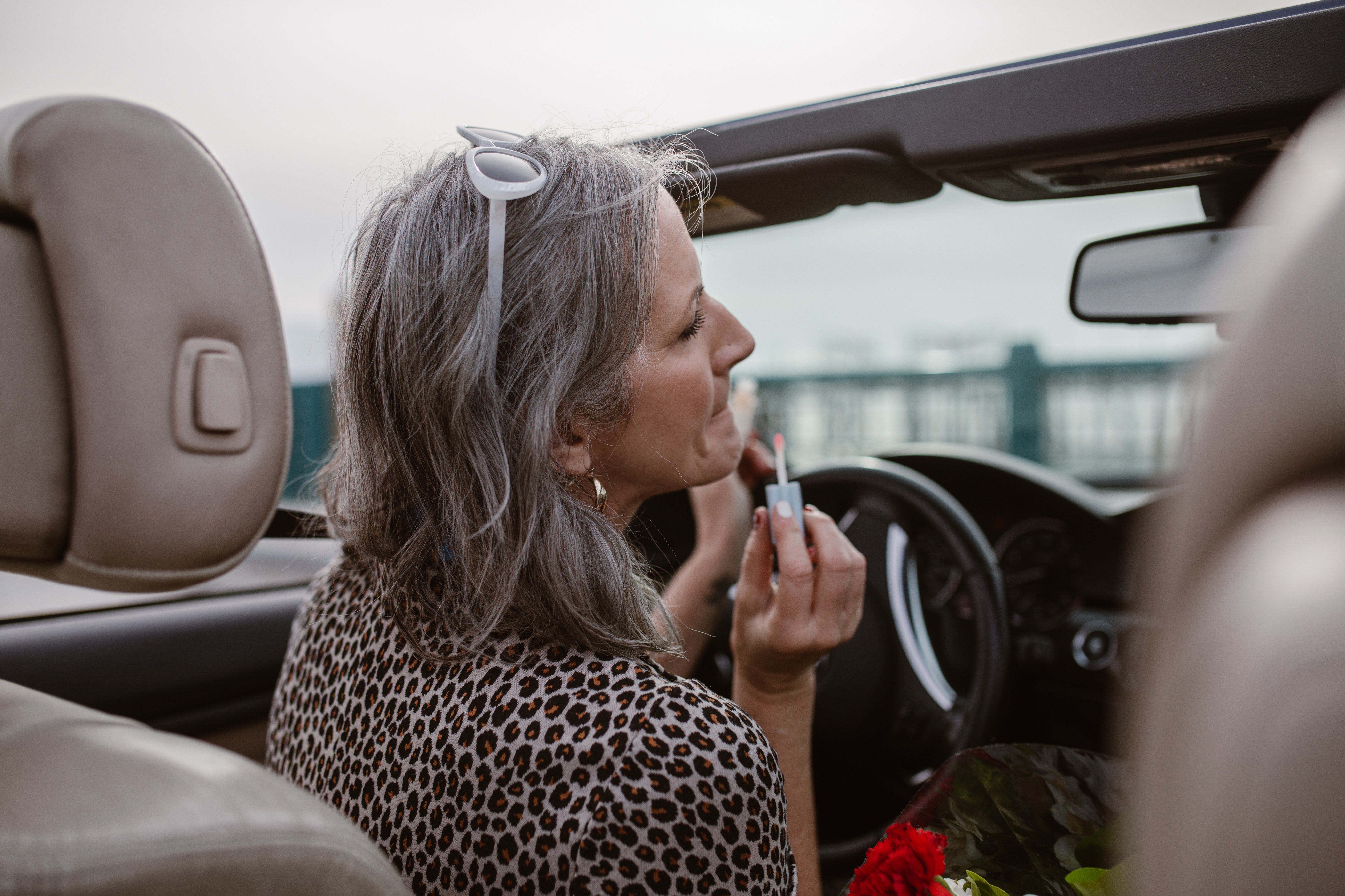A woman applying lip gloss in a brand-new car | Source: Pexels